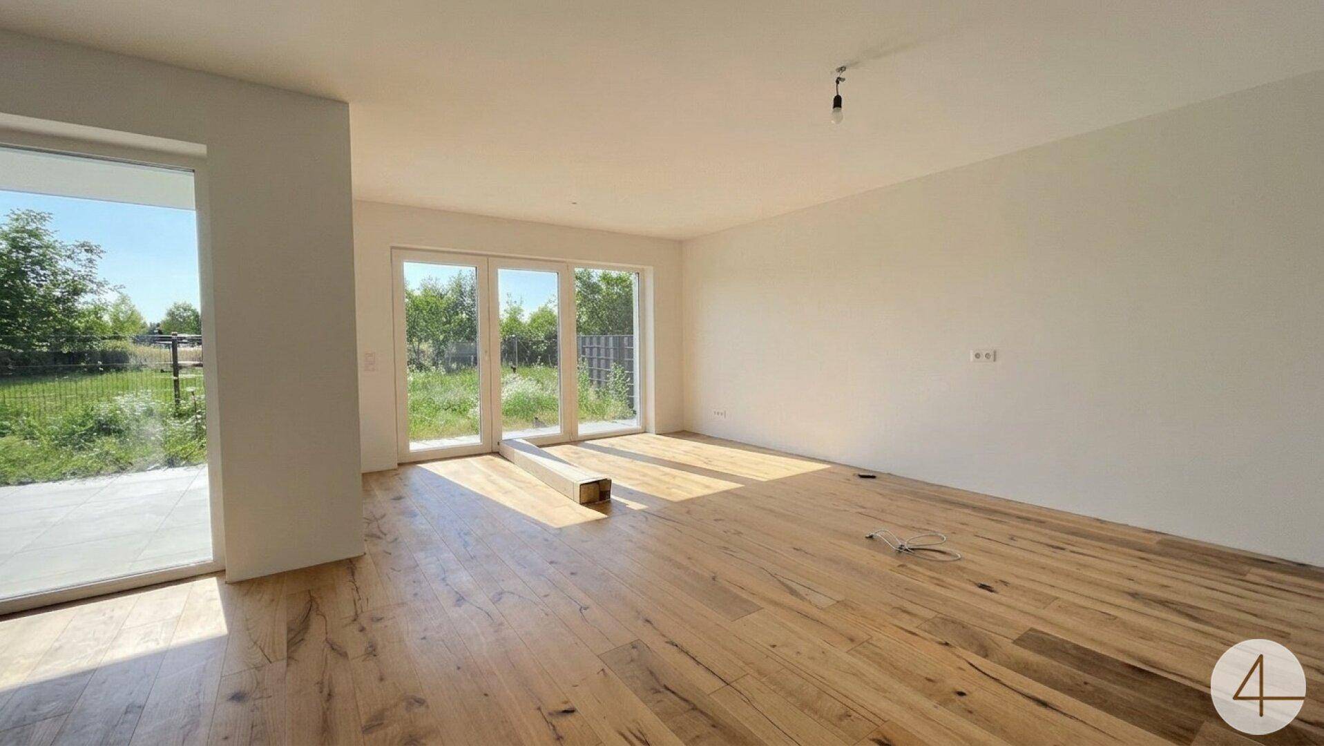 Geräumiger, heller Raum mit Holzboden und großen Fensterfronten, die einen weiten Blick in die Natur ermöglichen.