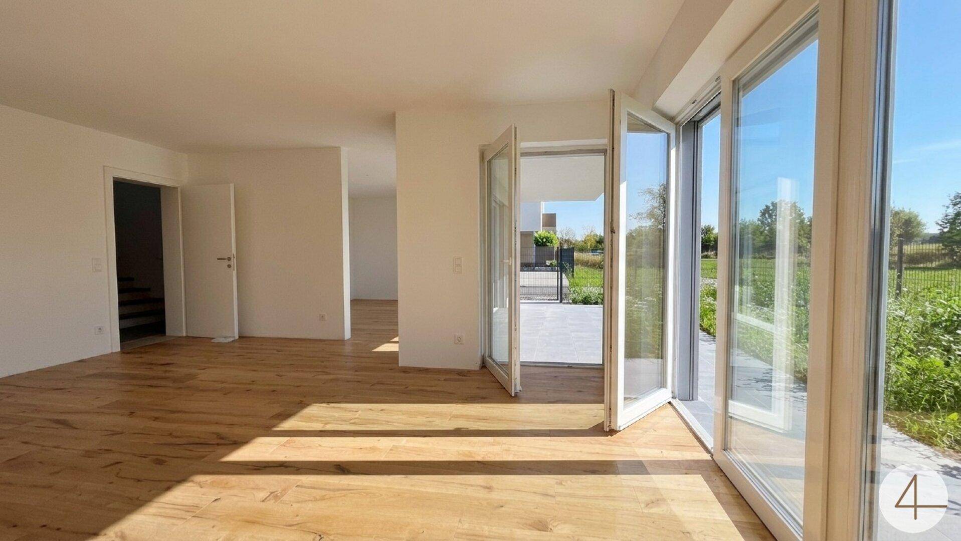 Heller Wohnbereich mit Holzboden und großen Fenstern, die den Blick ins Grüne freigeben und viel Licht spenden.