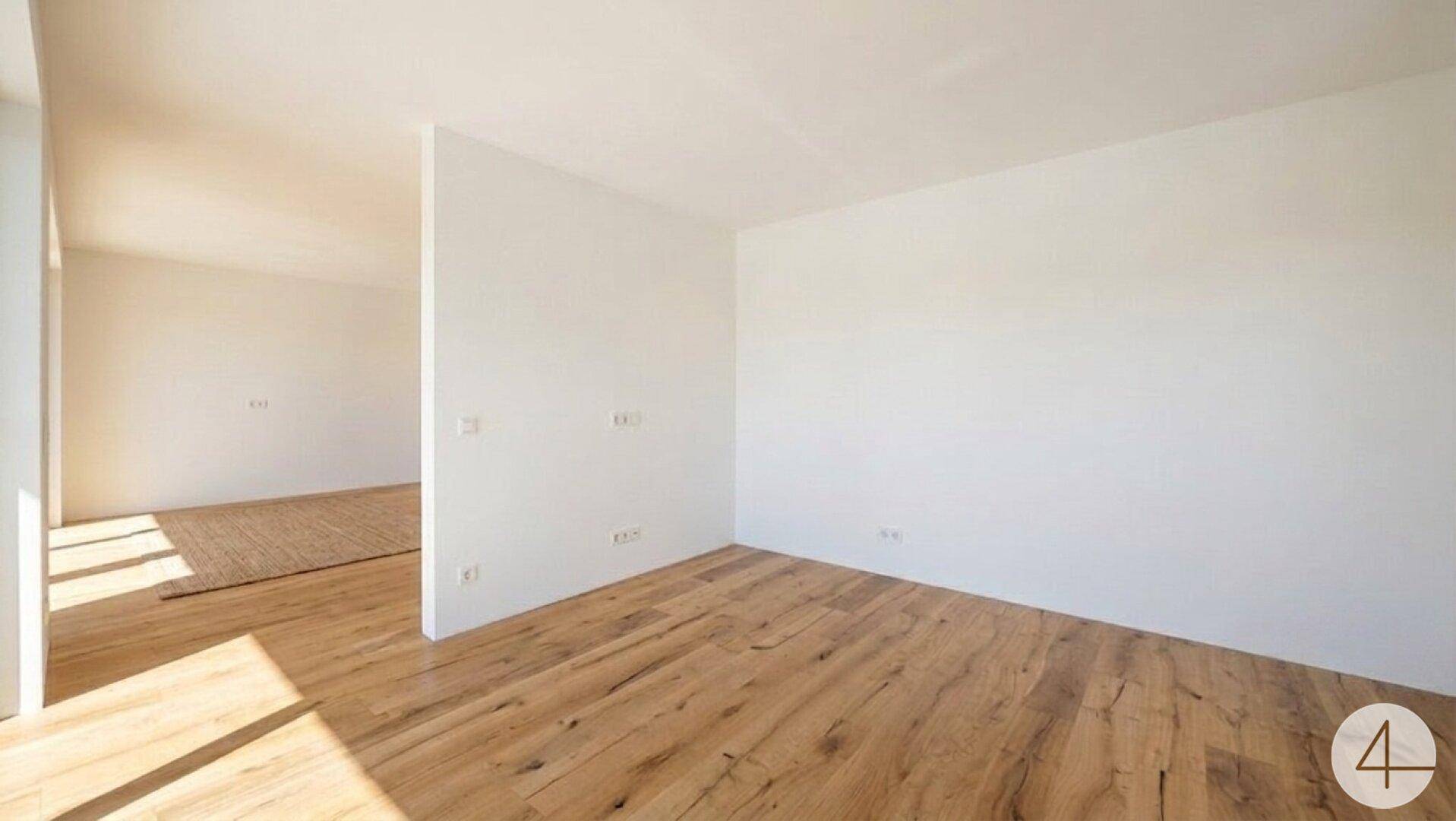 Heller Innenraum mit Holzboden und weißen Wänden, der vielseitig genutzt werden kann und natürliches Licht erhält.