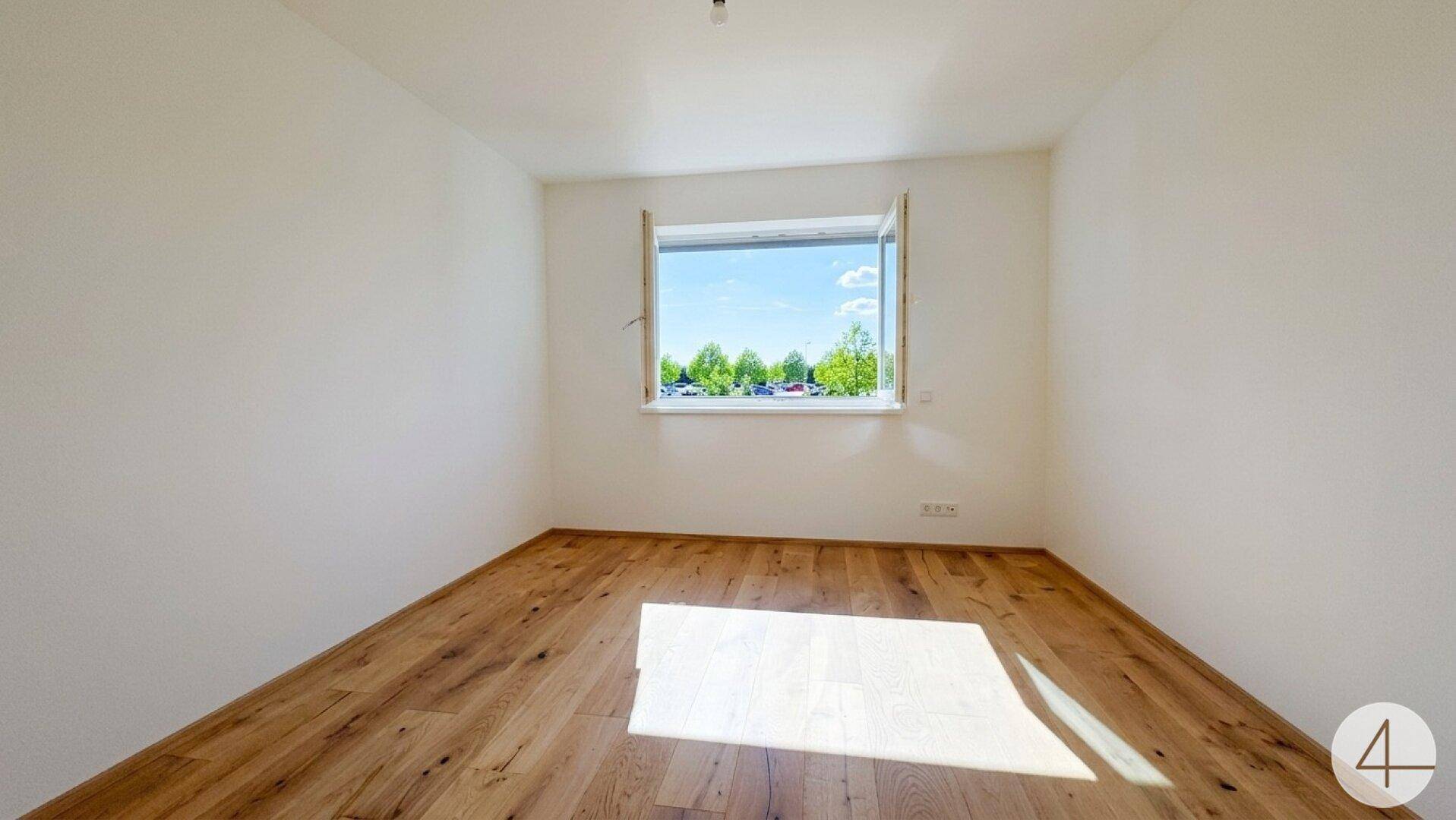 Helles Schlafzimmer mit Holzboden und einem Fenster, das einen Blick ins Grüne und auf die Umgebung bietet.
