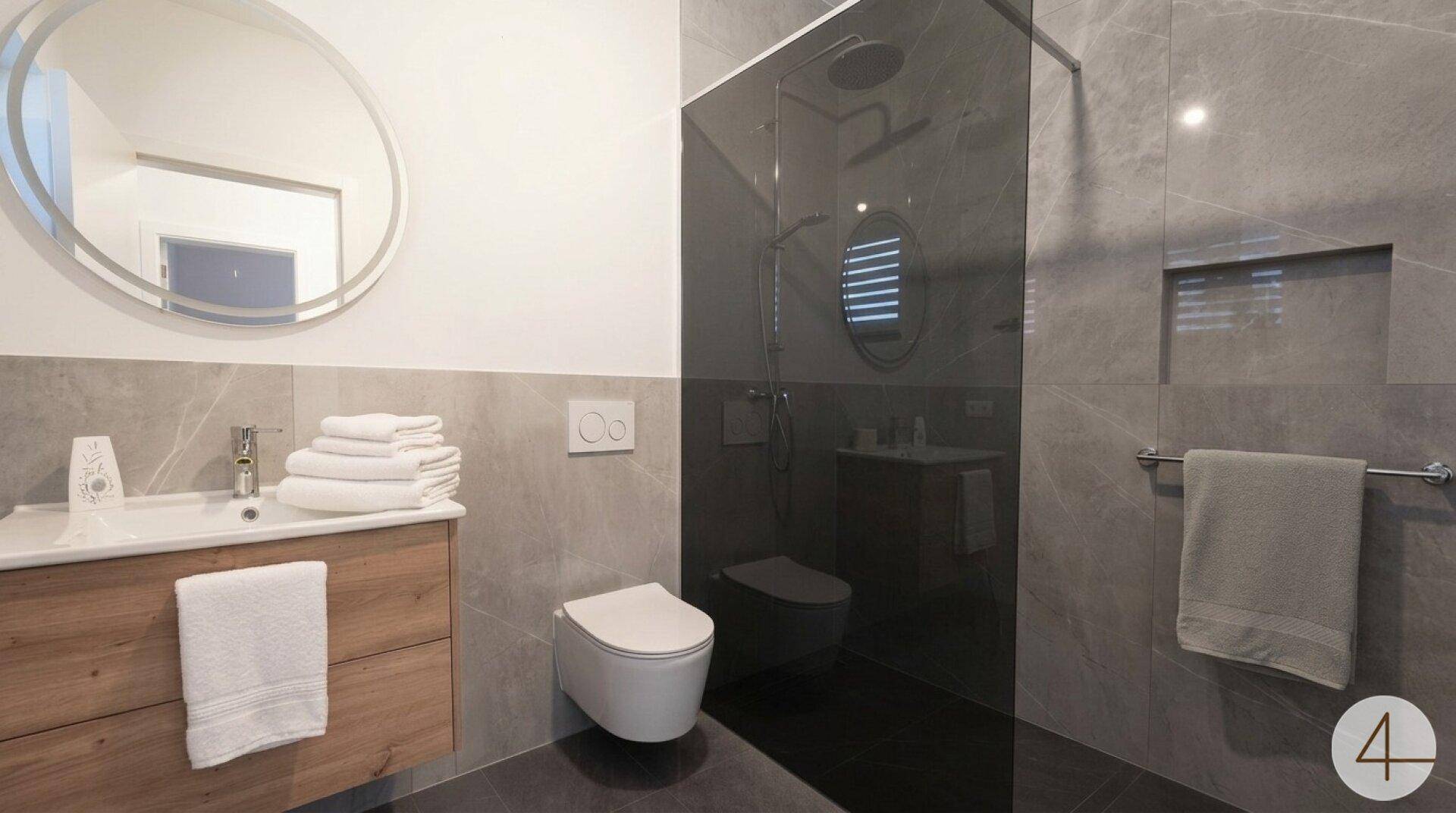 Modernes Badezimmer mit großformatigen grauen Fliesen, bodengleicher Dusche und Einzelwaschbecken.