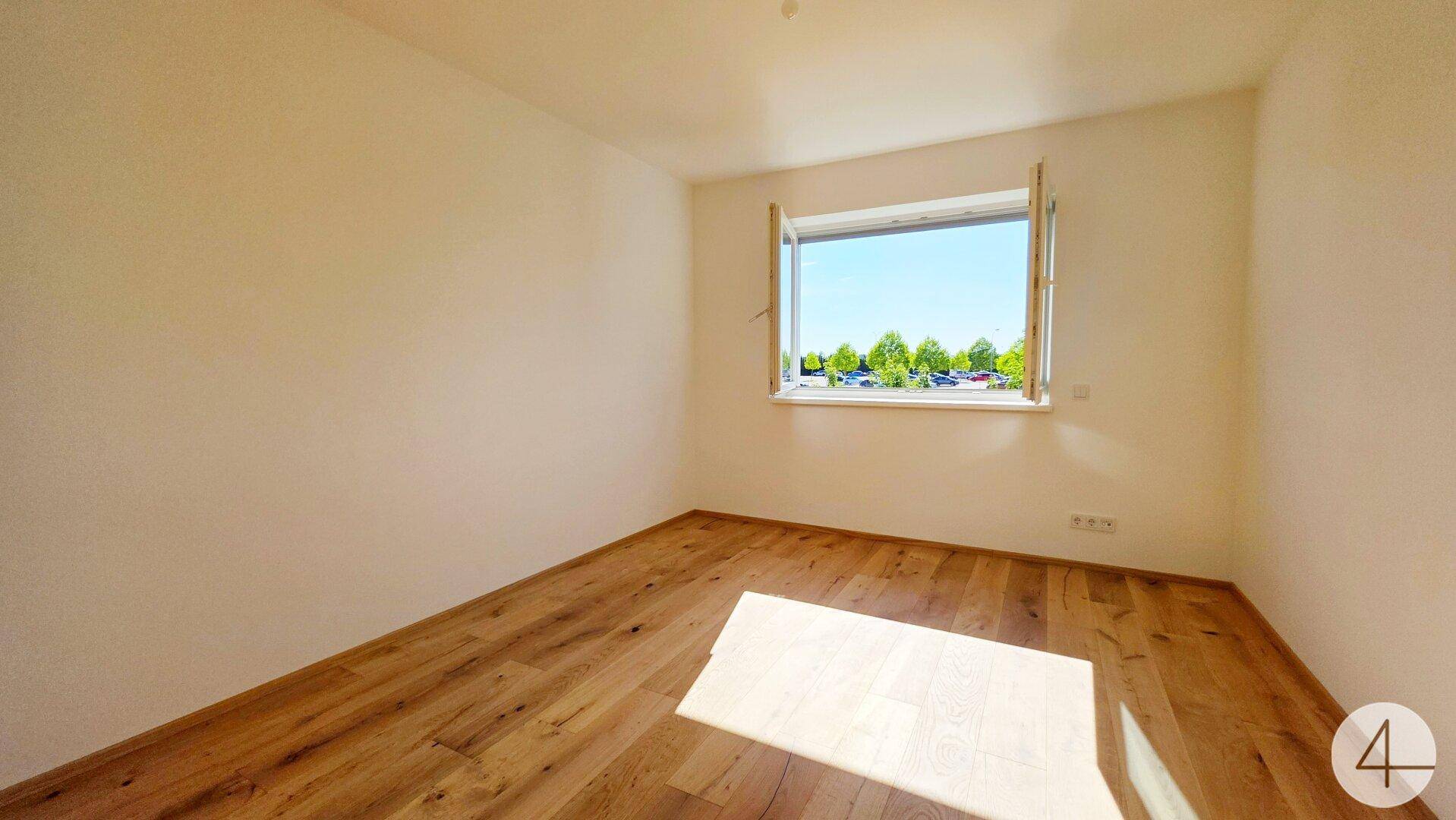 Helles Schlafzimmer mit Holzboden und Fenster mit Ausblick ins Grüne.
