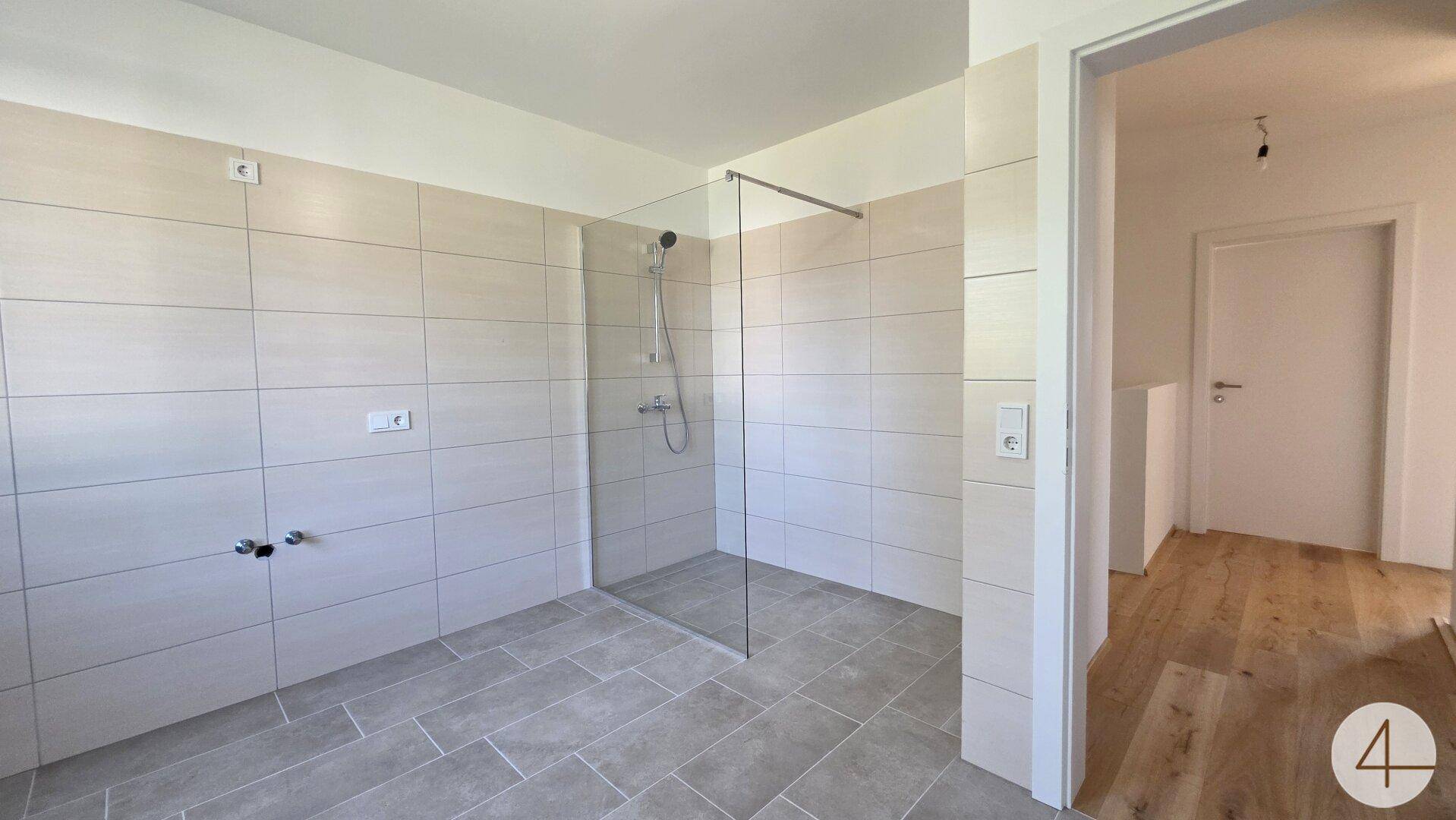 Modernes Badezimmer mit hellgrauen Fliesen und einer geräumigen begehbaren Dusche.