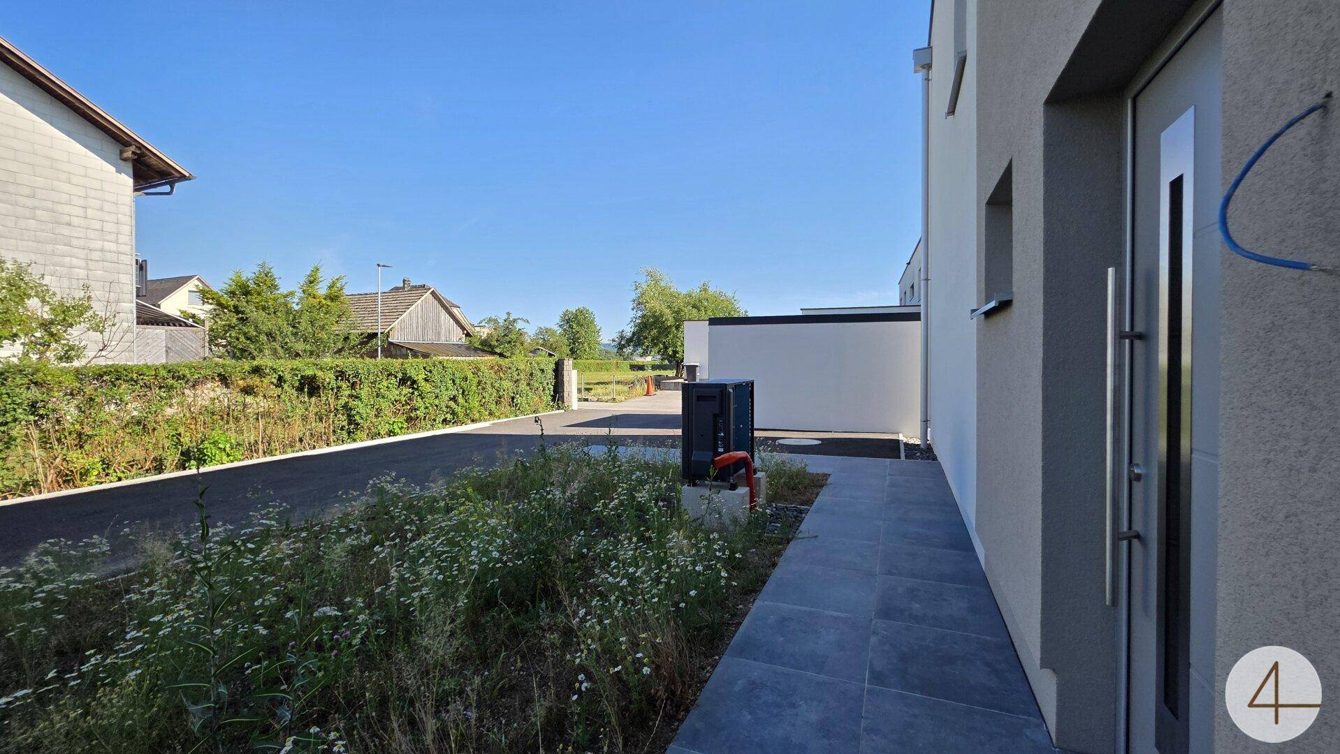 Eingangsbereich eines modernen Hauses mit gepflastertem Weg und Grünfläche.