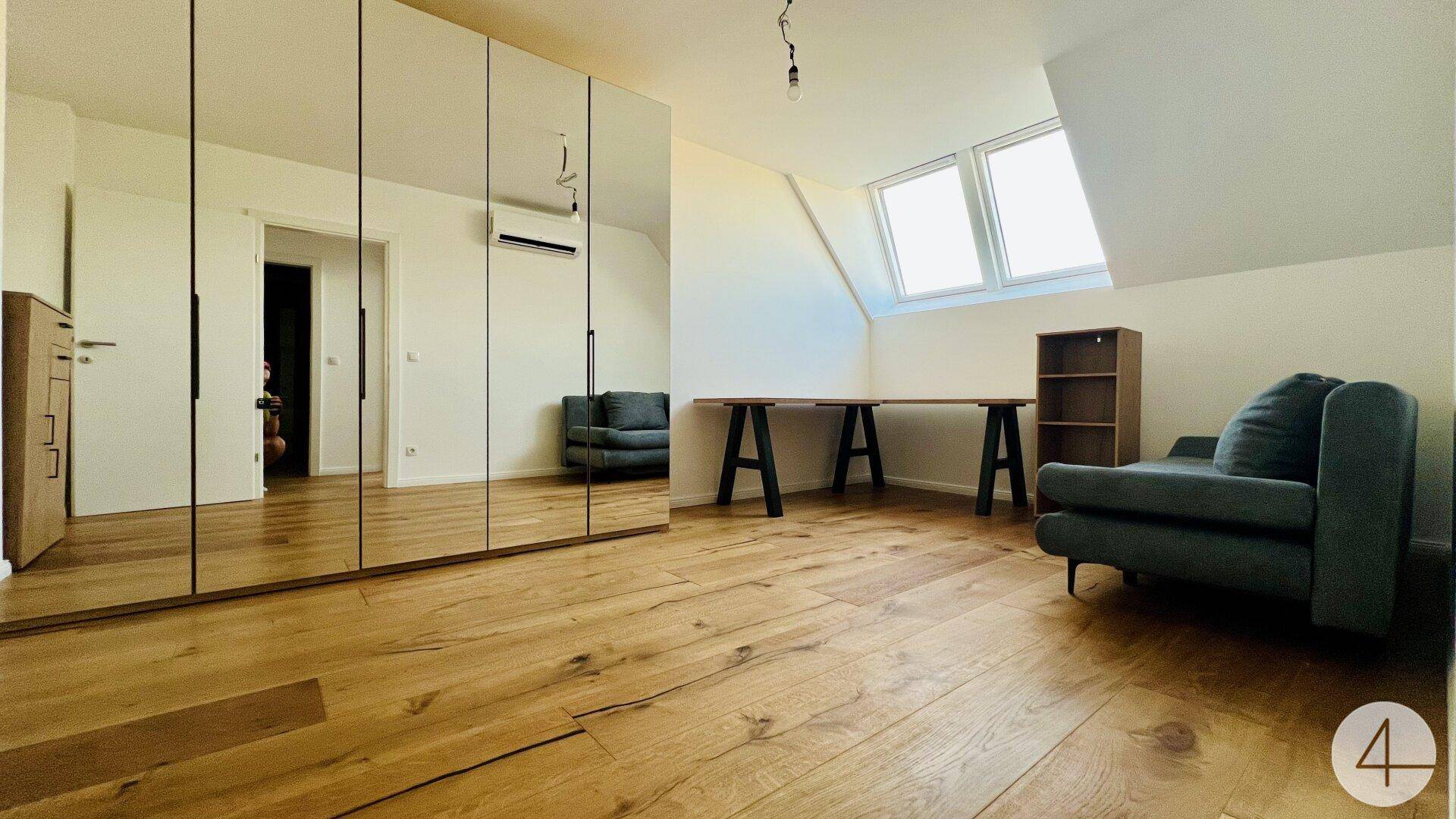 Helles Zimmer mit verspiegeltem Einbauschrank, Holzboden und Fenstern in der Dachschräge.