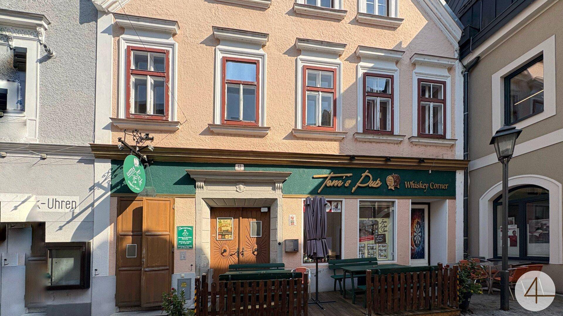 Fassade eines historischen Gebäudes mit dem Pub "Toni's Pub" im Erdgeschoss und Außensitzbereich.