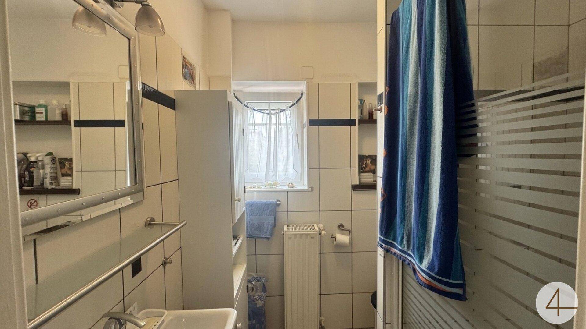 Helles Badezimmer mit weißen Fliesen, Dusche und Fenster.