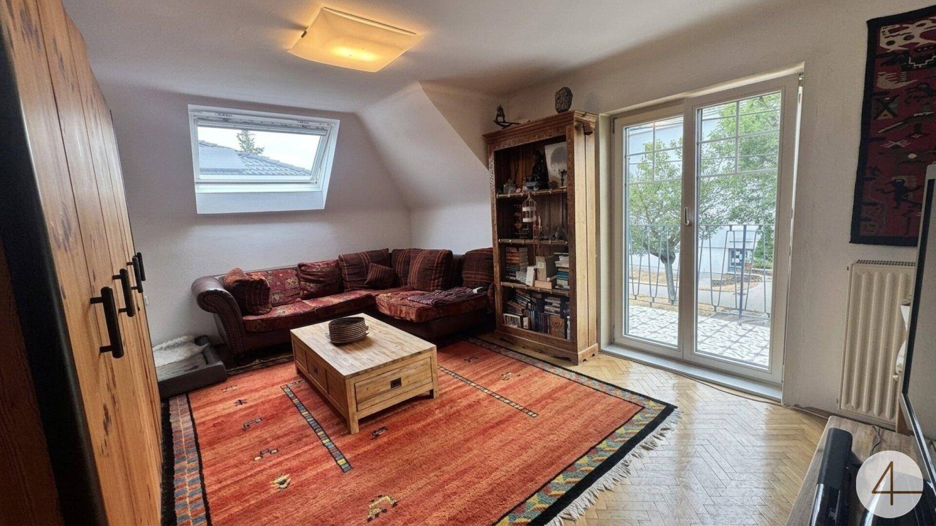 Gemütliches Wohnzimmer im Dachgeschoss mit Sofa, Teppich und Zugang zum Balkon.