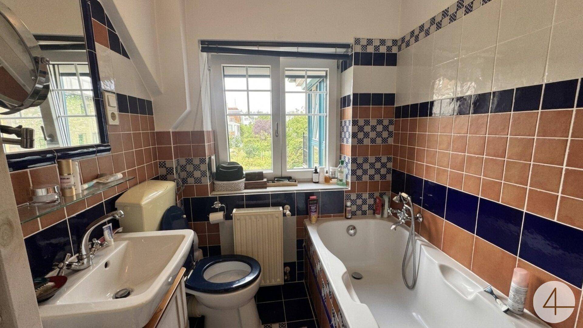 Badezimmer mit Badewanne, WC und farbigen Fliesen in Blau und Braun.