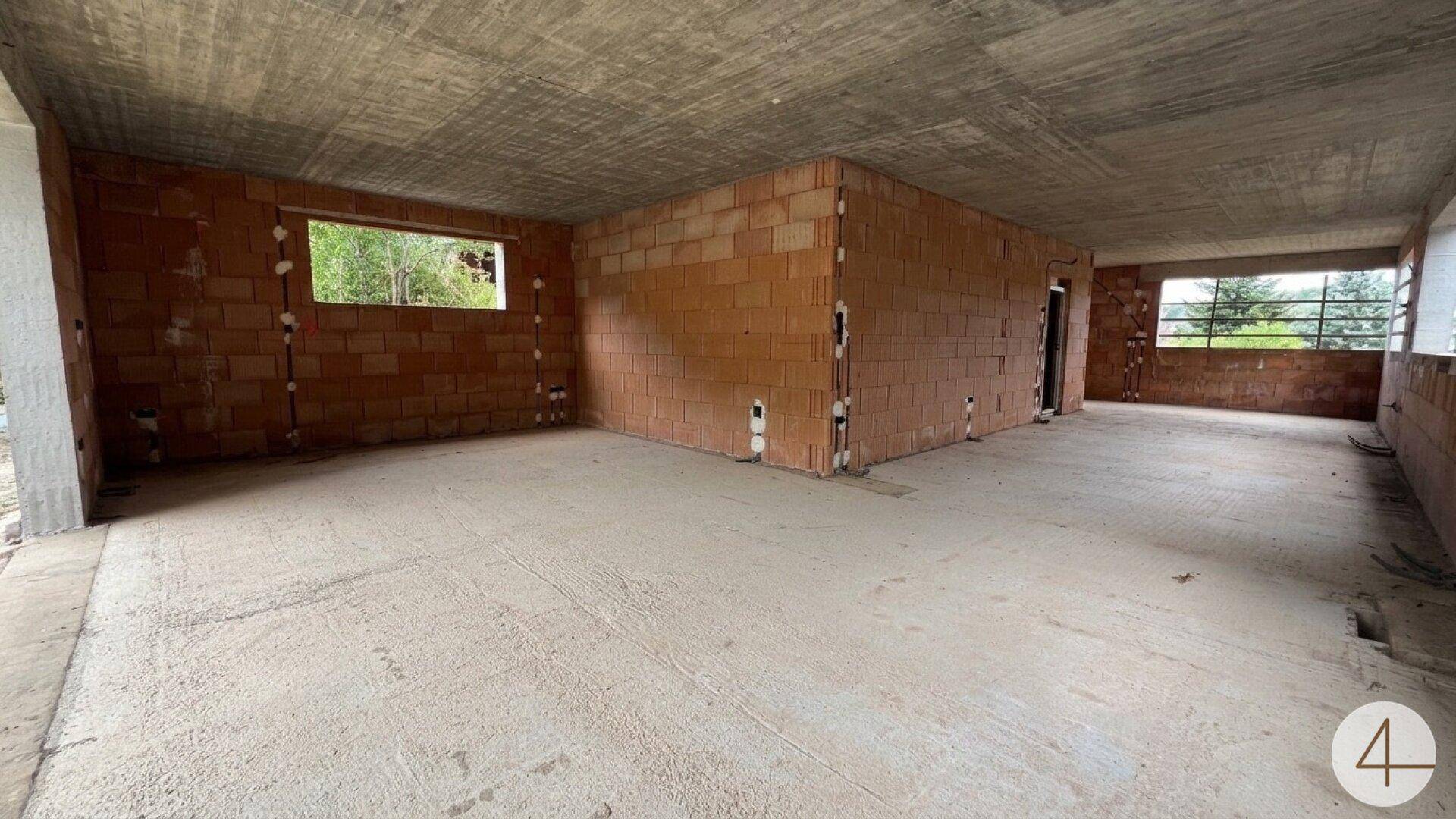 Unfertiger Innenraum mit unverputzten Ziegelwänden, Betonboden und großen Fensteröffnungen.