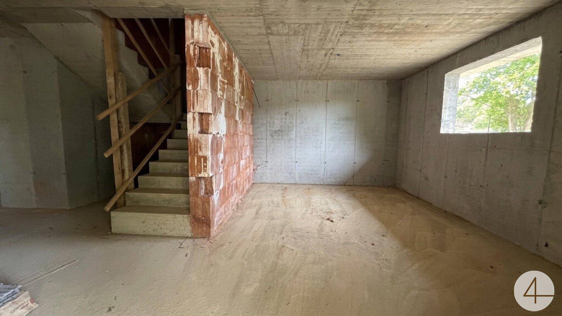 Unfertiger Kellerraum mit Betontreppe und einem Fenster, das Tageslicht hereinlässt.