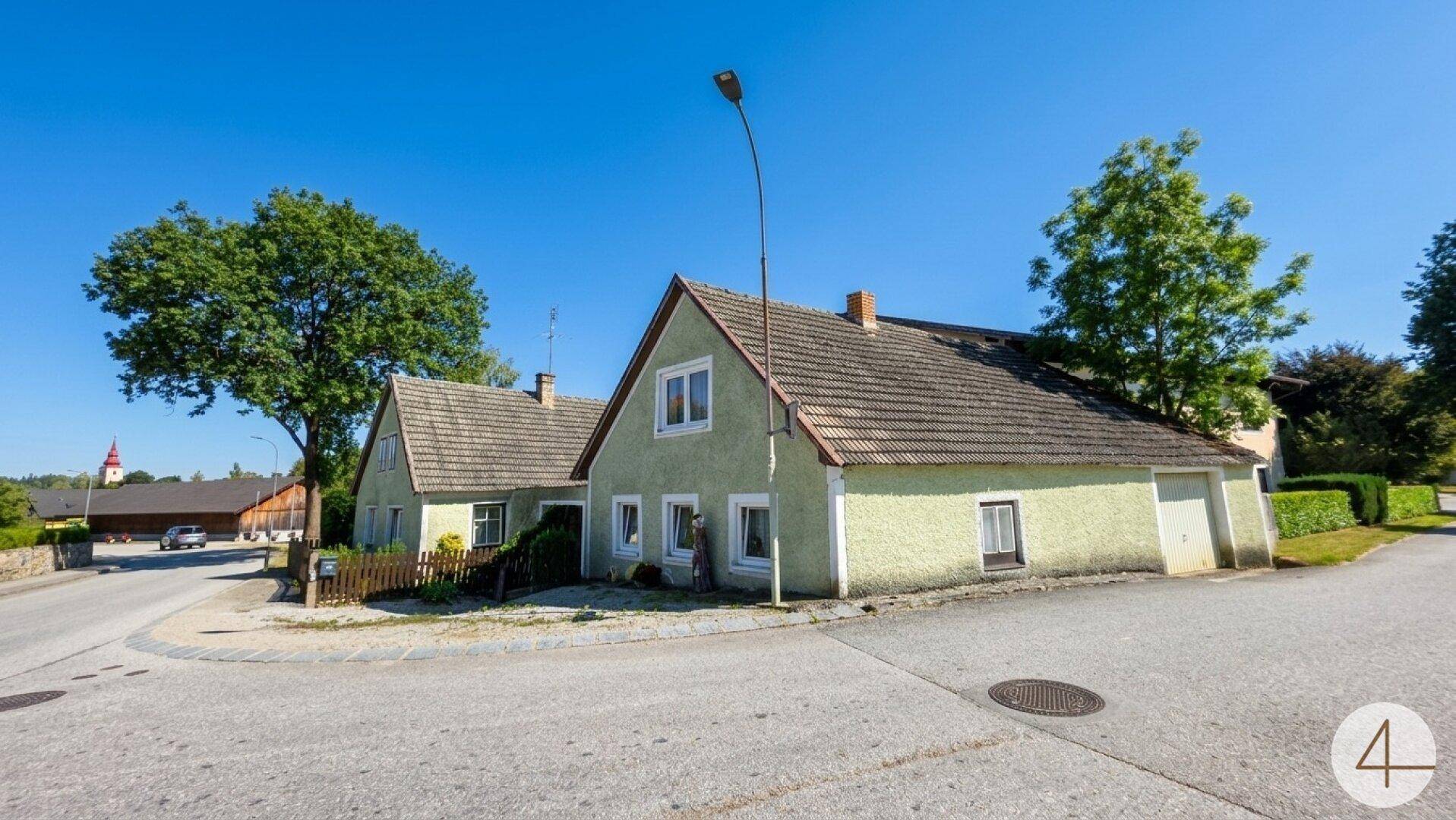 Seitenansicht des Hauses mit hellgrüner Fassade, Ziegeldach und angrenzender Straße.