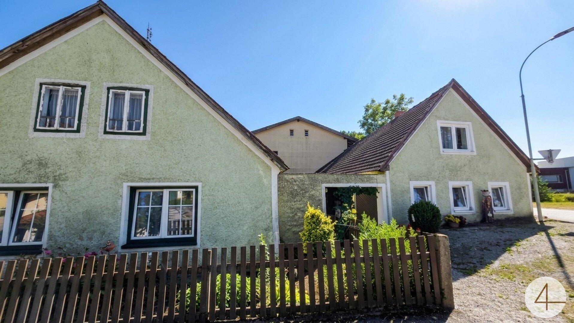 Nahaufnahme der hellgrünen Fassade des Hauses mit Holzzaun und kleinen Fenstern.