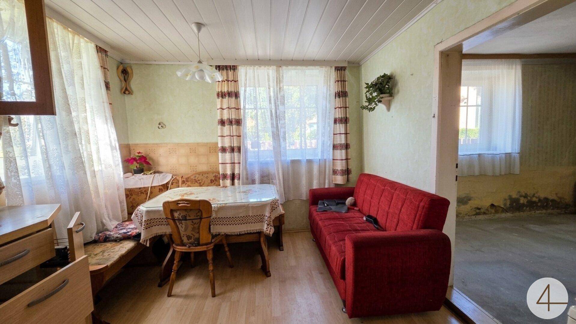 Gemütlicher Wohn-Essbereich mit rotem Sofa, Esstisch und hellen Fenstern.
