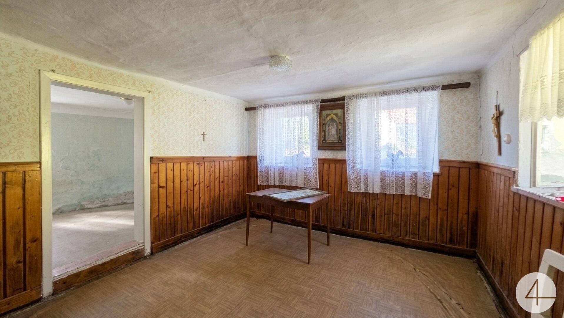 Wohnraum mit Holzvertäfelung, gemusterter Tapete und einem kleinen Tisch in der Mitte.
