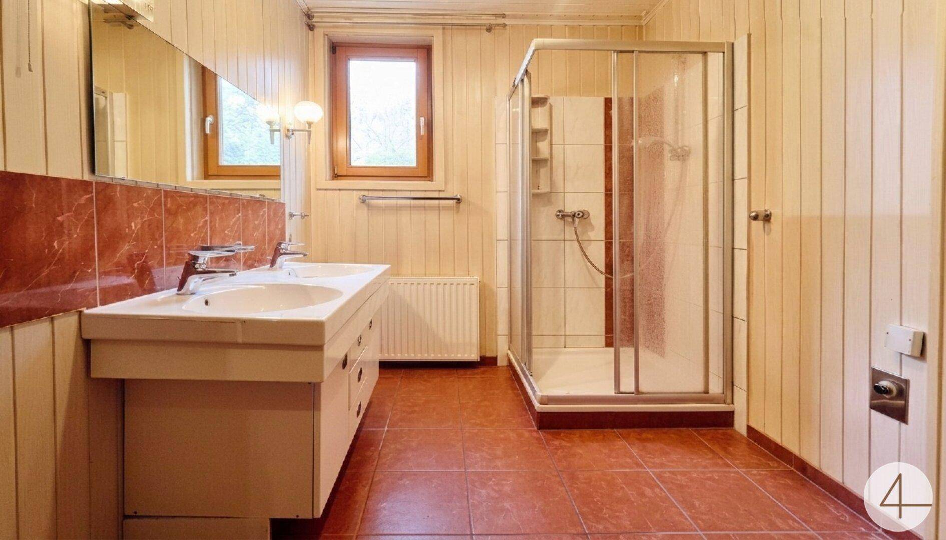 Badezimmer mit Doppelwaschbecken, Duschkabine, terracottafarbenen Fliesen und Holzvertäfelung an den Wänden.