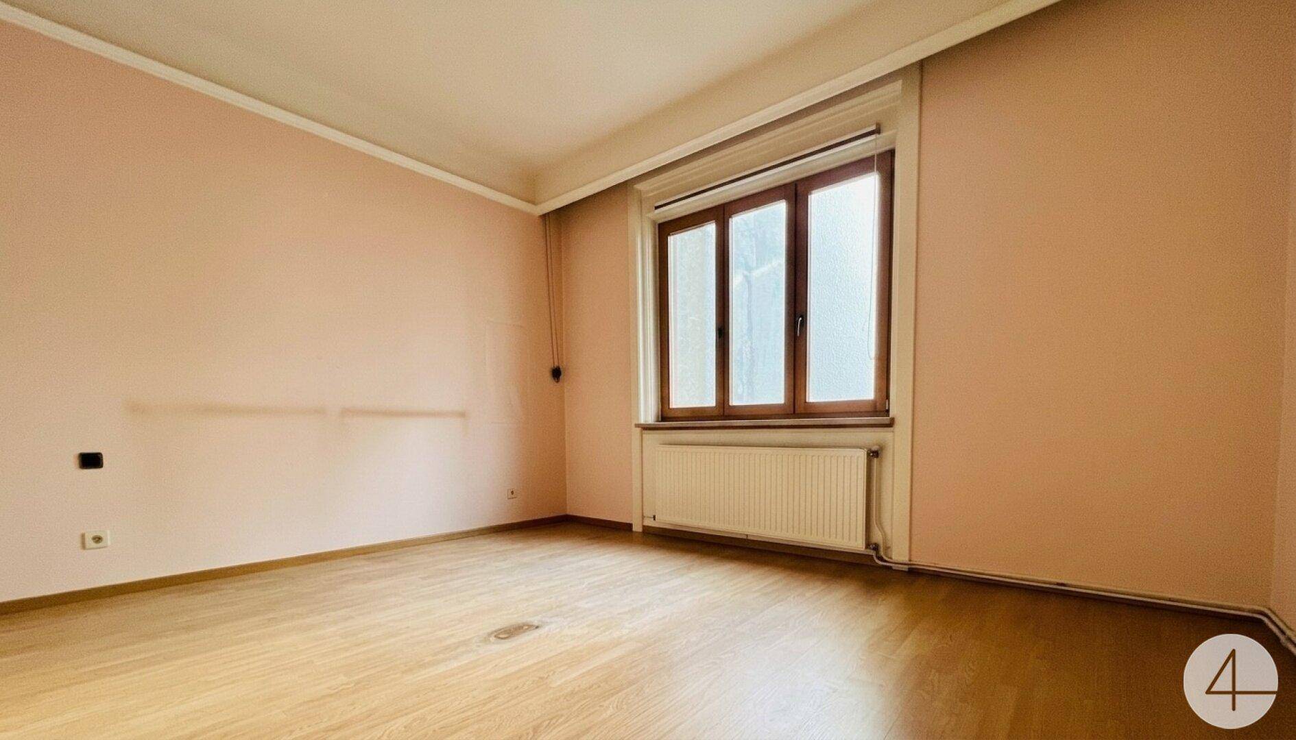Geräumiges Schlafzimmer mit hellrosa Wänden, Holzfußboden und einem Fenster mit Holzrahmen.