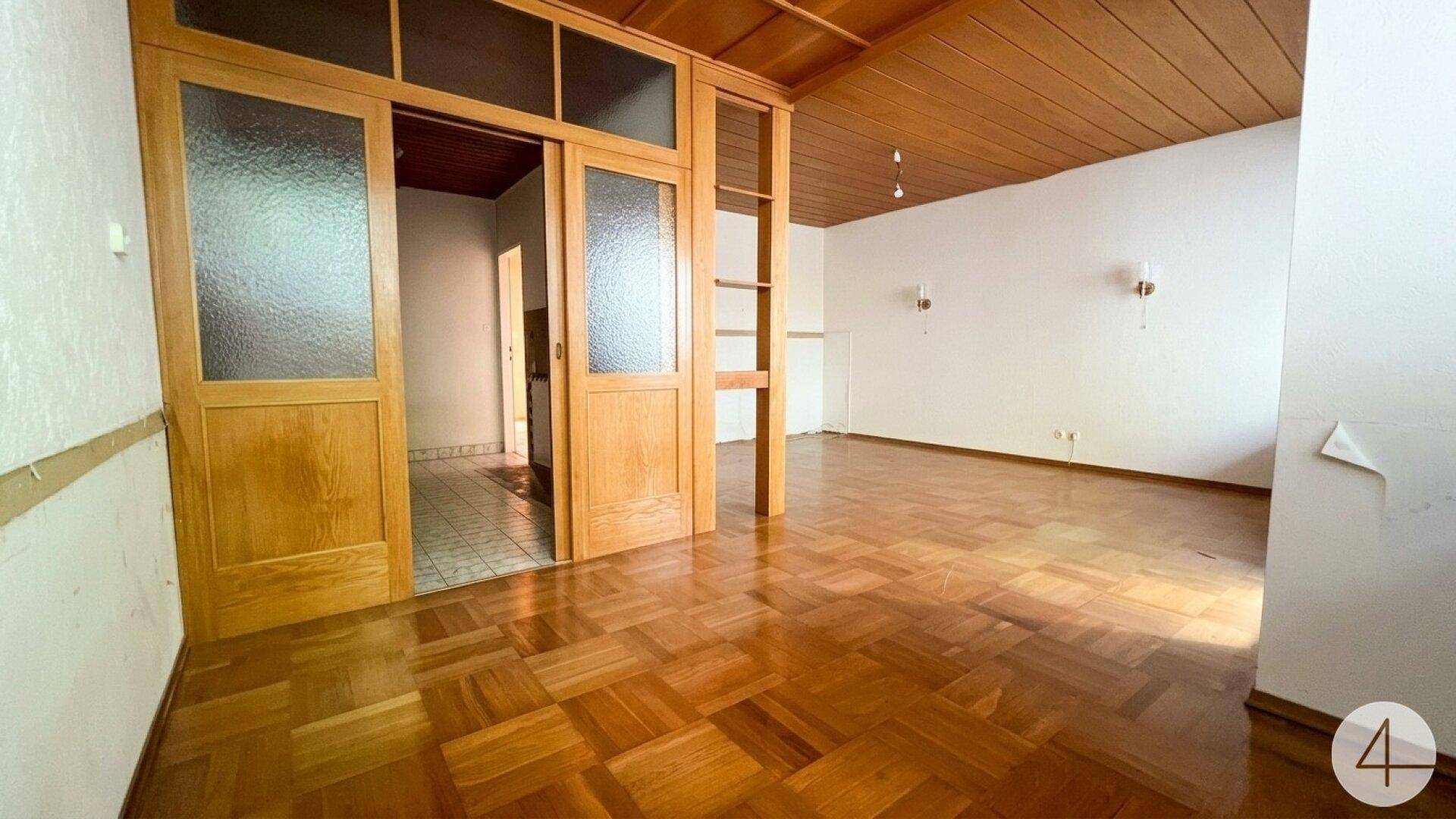 Geräumiges Wohnzimmer mit Holzparkettboden, Holzdecke und Schiebetüren zu einem weiteren Raum.