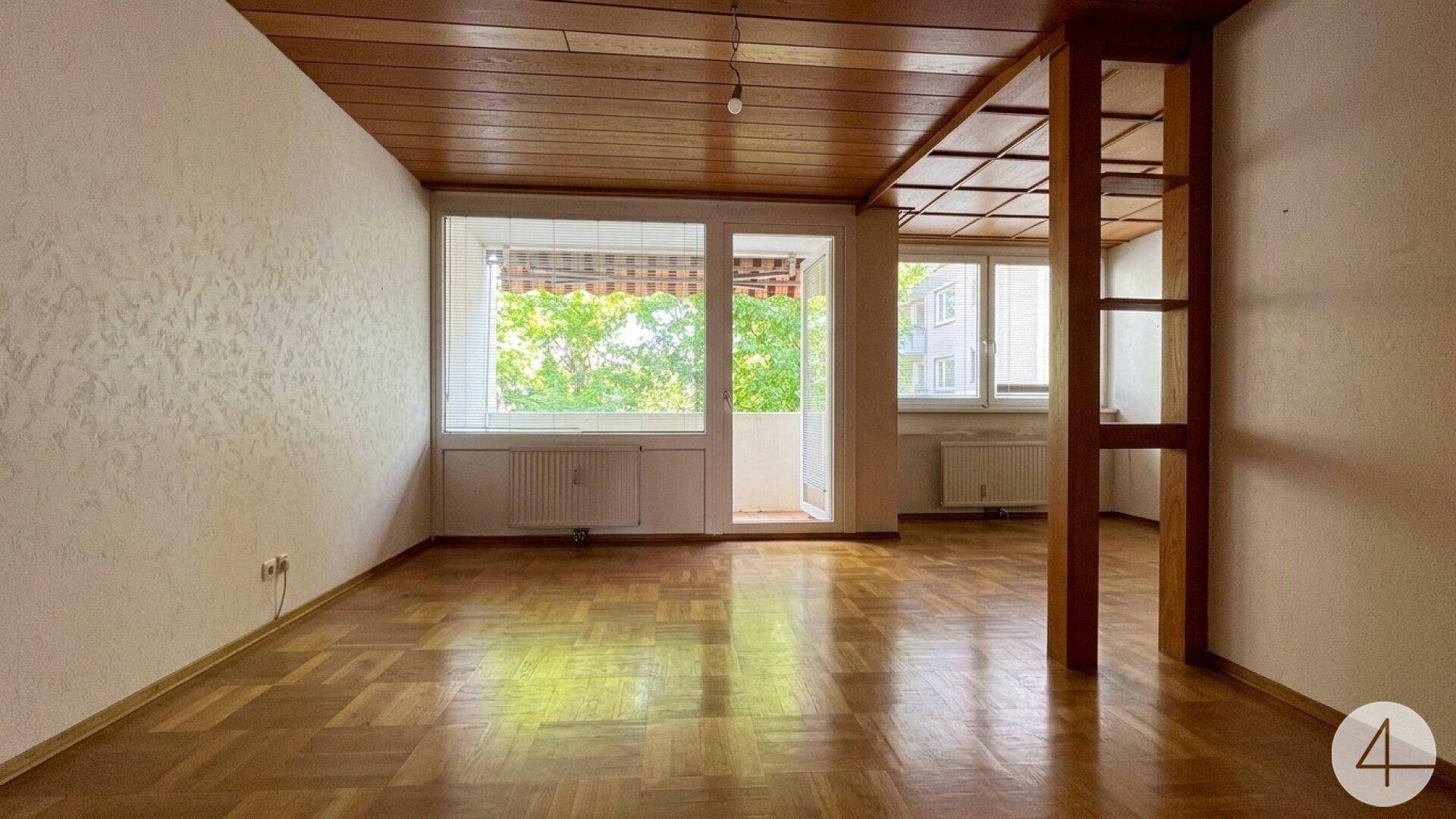Helles Wohnzimmer mit Parkettboden, Holzdecke und Zugang zu einem kleinen Balkon.