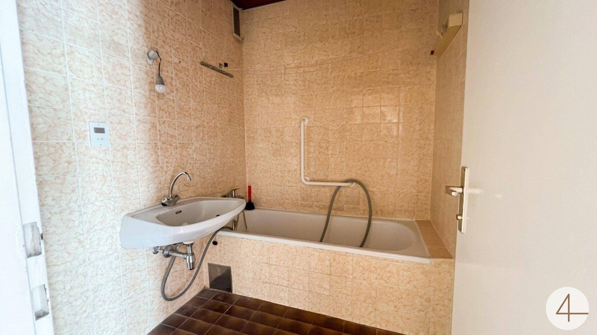 Badezimmer mit beigefarbenen Fliesen, Badewanne und Waschbecken, renovierungsbedürftig.