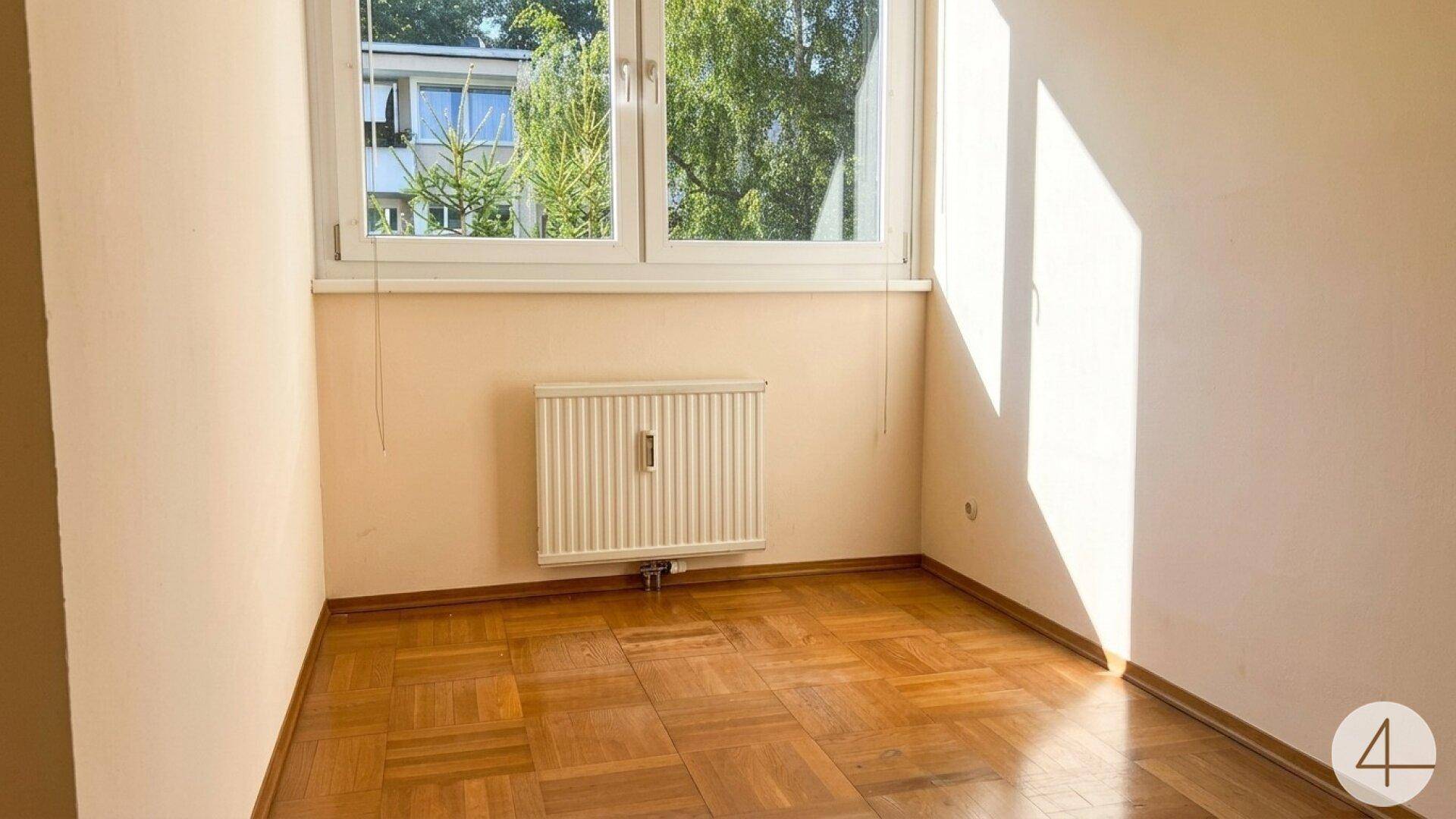 Helles Schlafzimmer mit Parkettboden und großem Fenster, das viel Tageslicht hereinlässt.