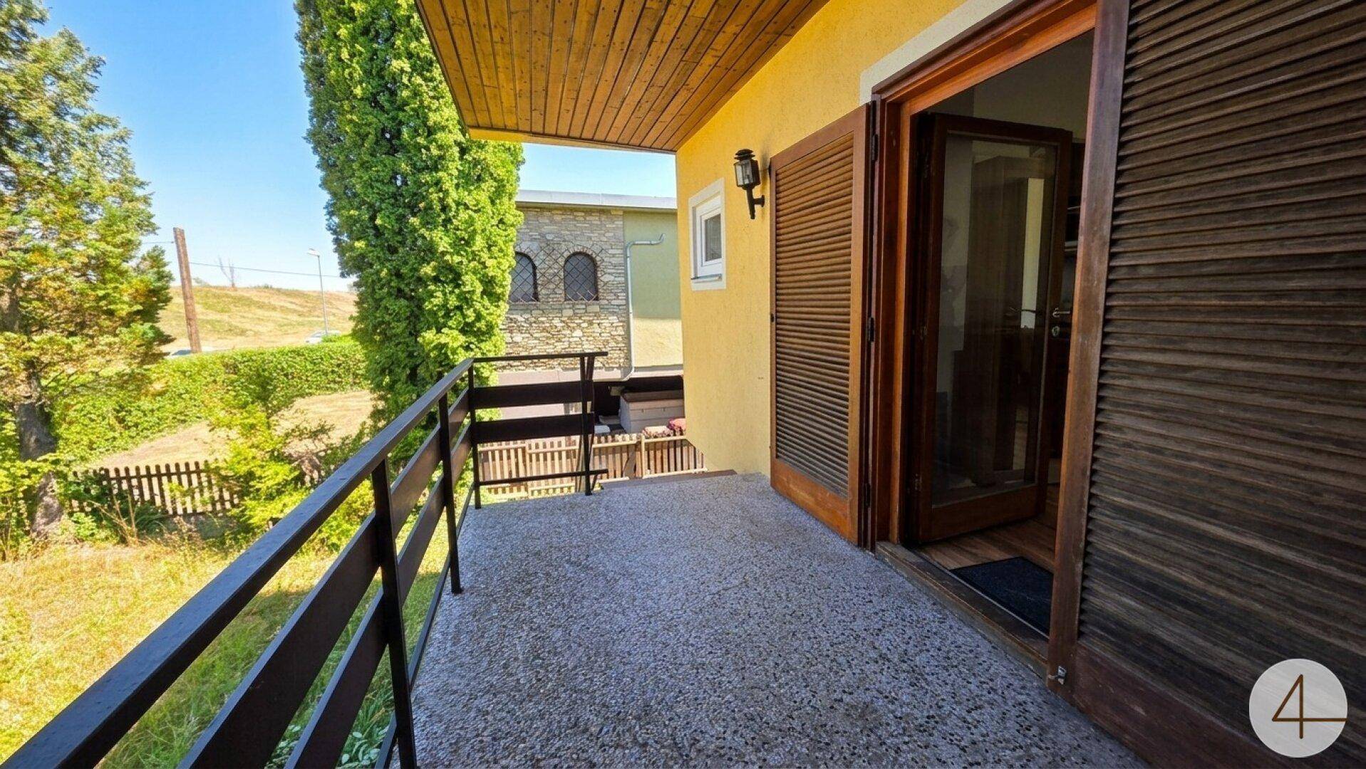 Balkon mit dunklem Geländer und Holzdach, bietet einen Blick auf die grüne Umgebung.