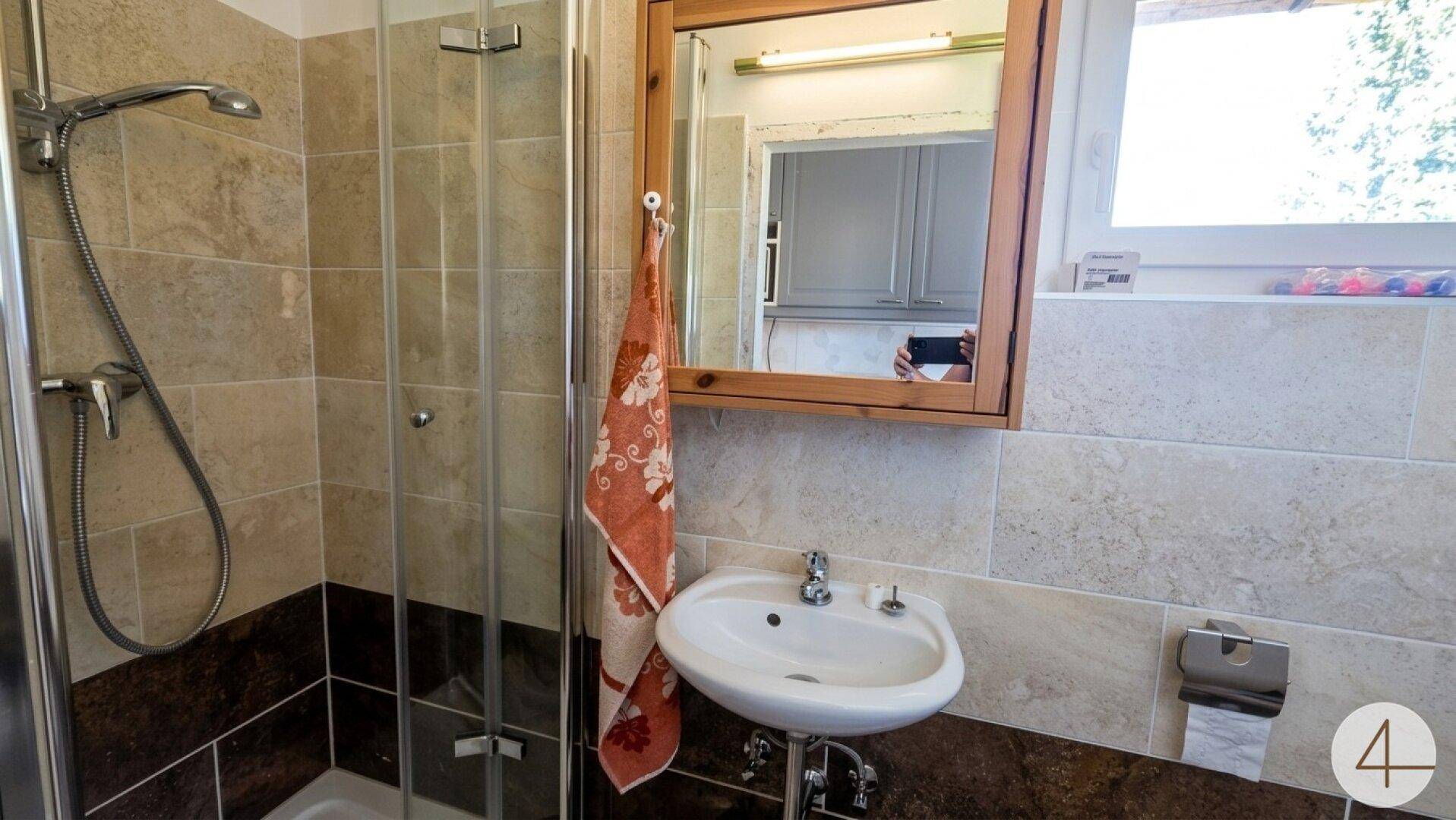 Badezimmer mit Duschkabine, Waschbecken und Spiegelschrank, gefliest in Erdtönen.