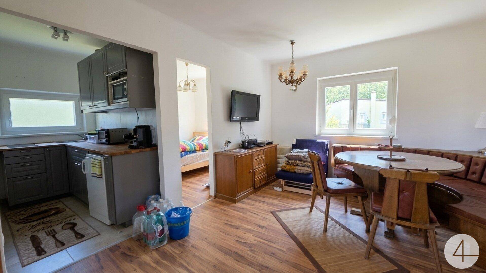 Offener Wohnbereich mit integrierter Küche, Esstisch und Zugang zu einem Schlafzimmer.