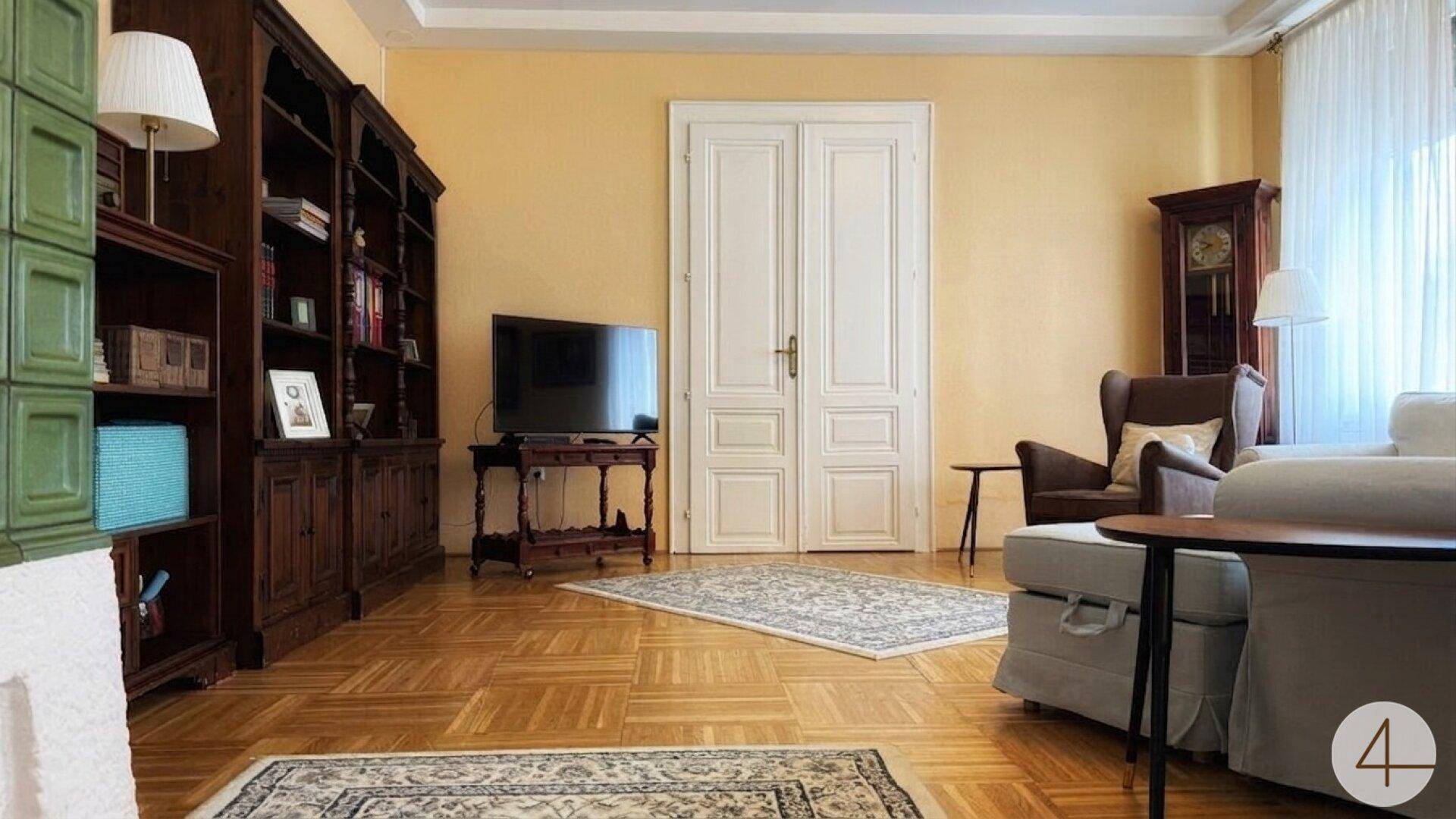 Gemütliches Wohnzimmer mit Fischgrätparkett, großem Bücherregal, Fernseher und klassischer Doppeltür.