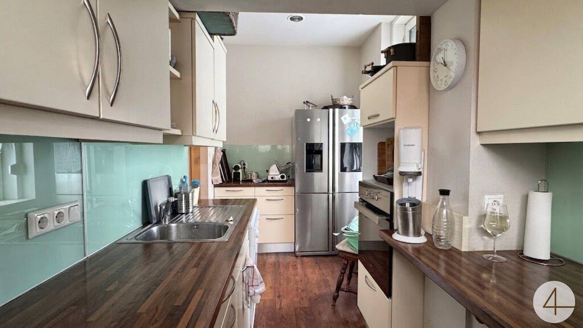 Helle Küche mit Holz-Arbeitsplatten, beigen Schränken und einem modernen Kühlschrank.