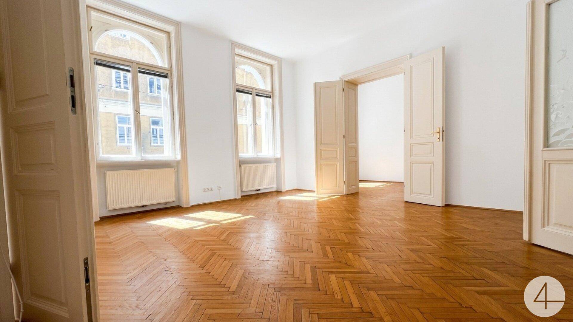 Geräumiges Zimmer mit klassischem Fischgrätparkett und großen Bogenfenstern, die viel Licht hereinlassen.