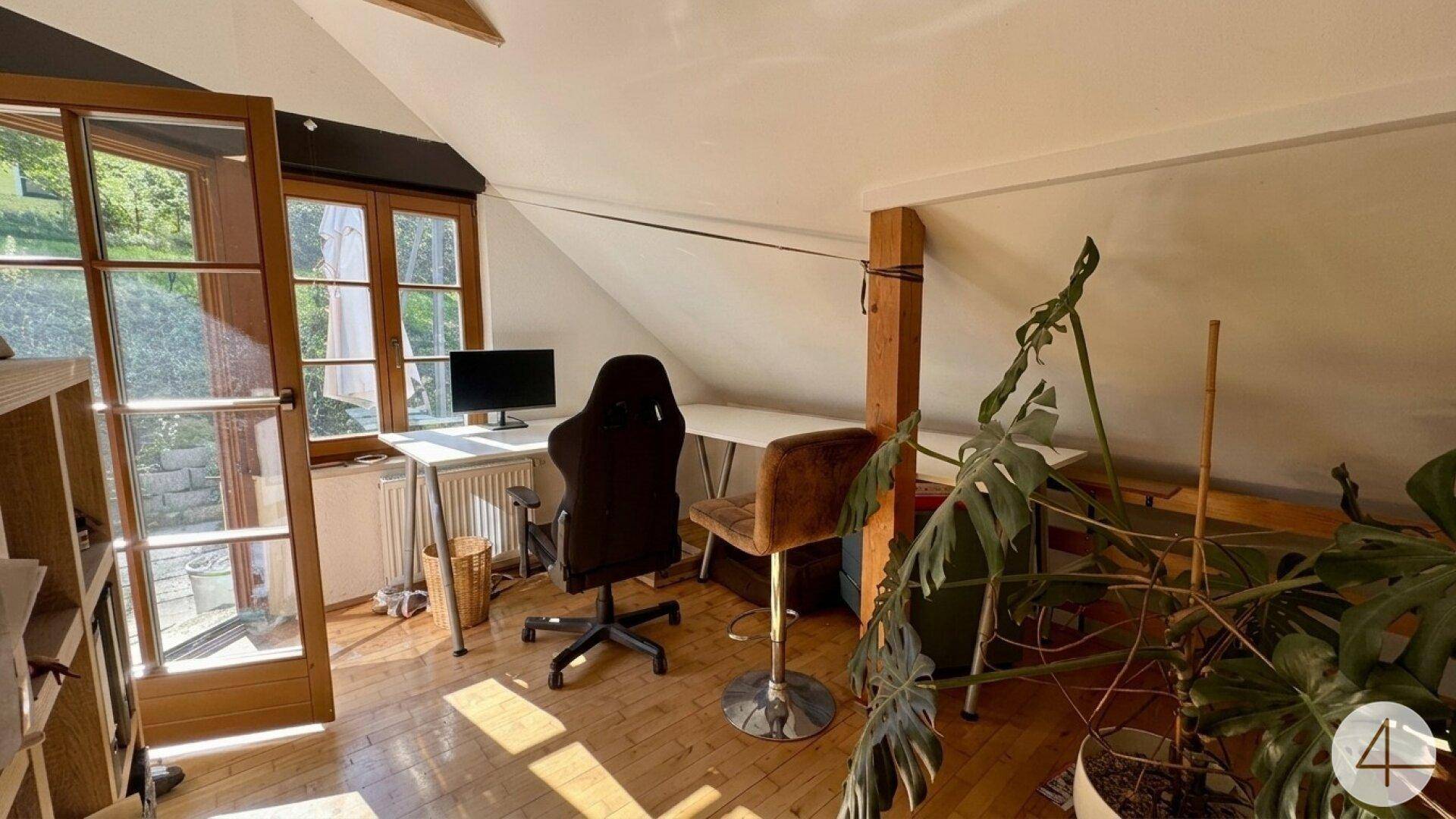 Helles Dachgeschoss-Büro mit Holzboden, Schreibtisch und Zugang zum Außenbereich.