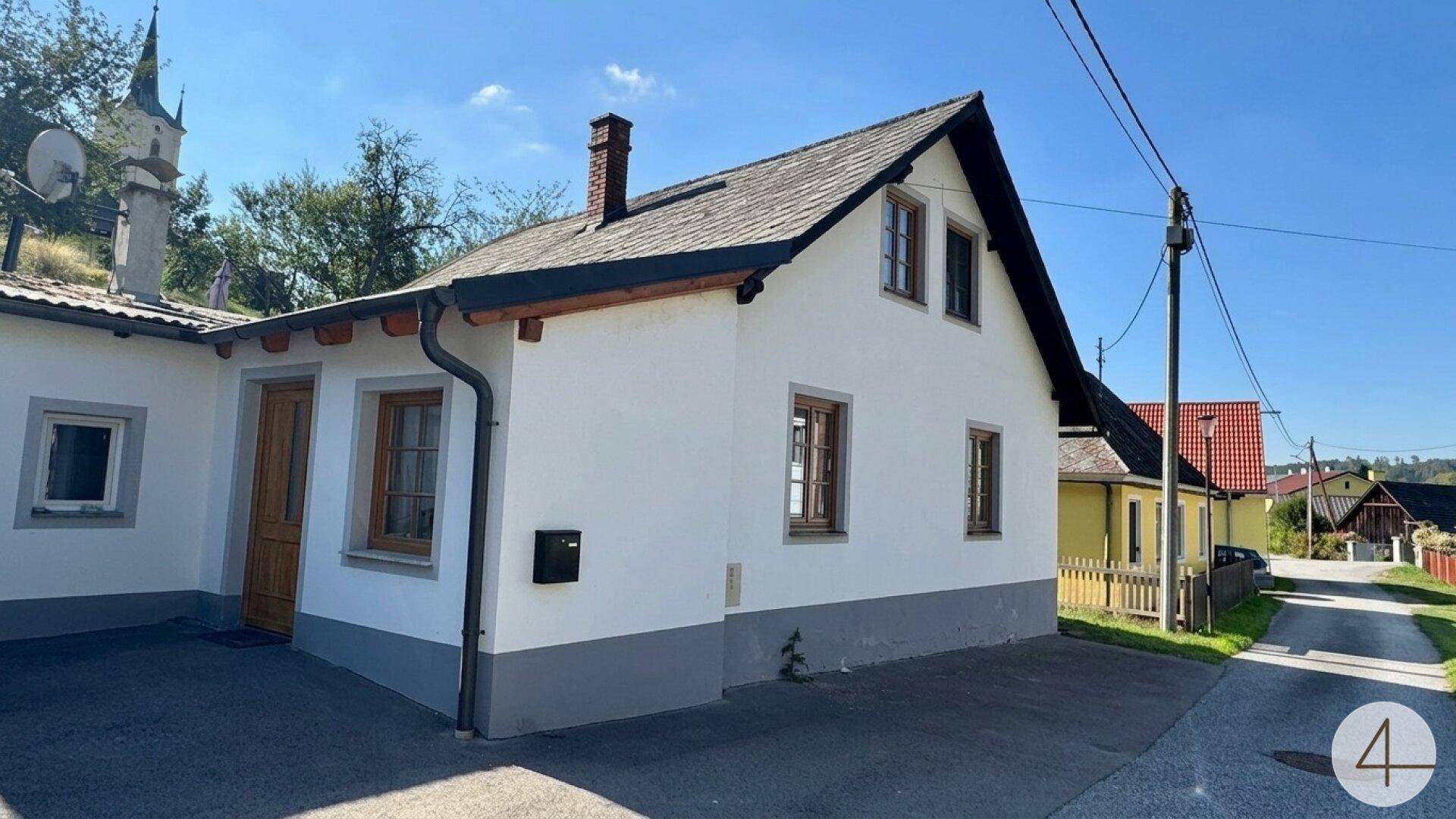 Traditionelles Einfamilienhaus mit weißer Fassade, Satteldach und Holzelementen.