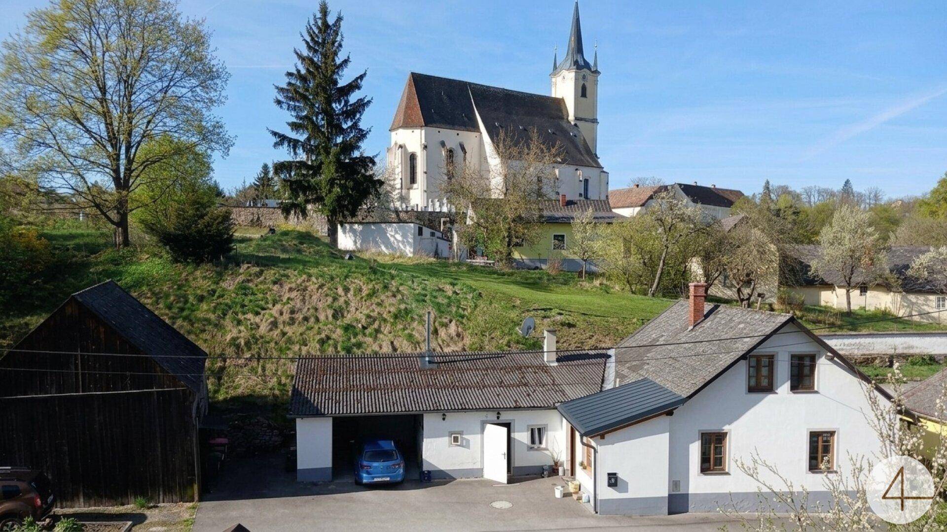 Malerische Dorfansicht mit Kirche, Wohnhäusern und grüner Landschaft.