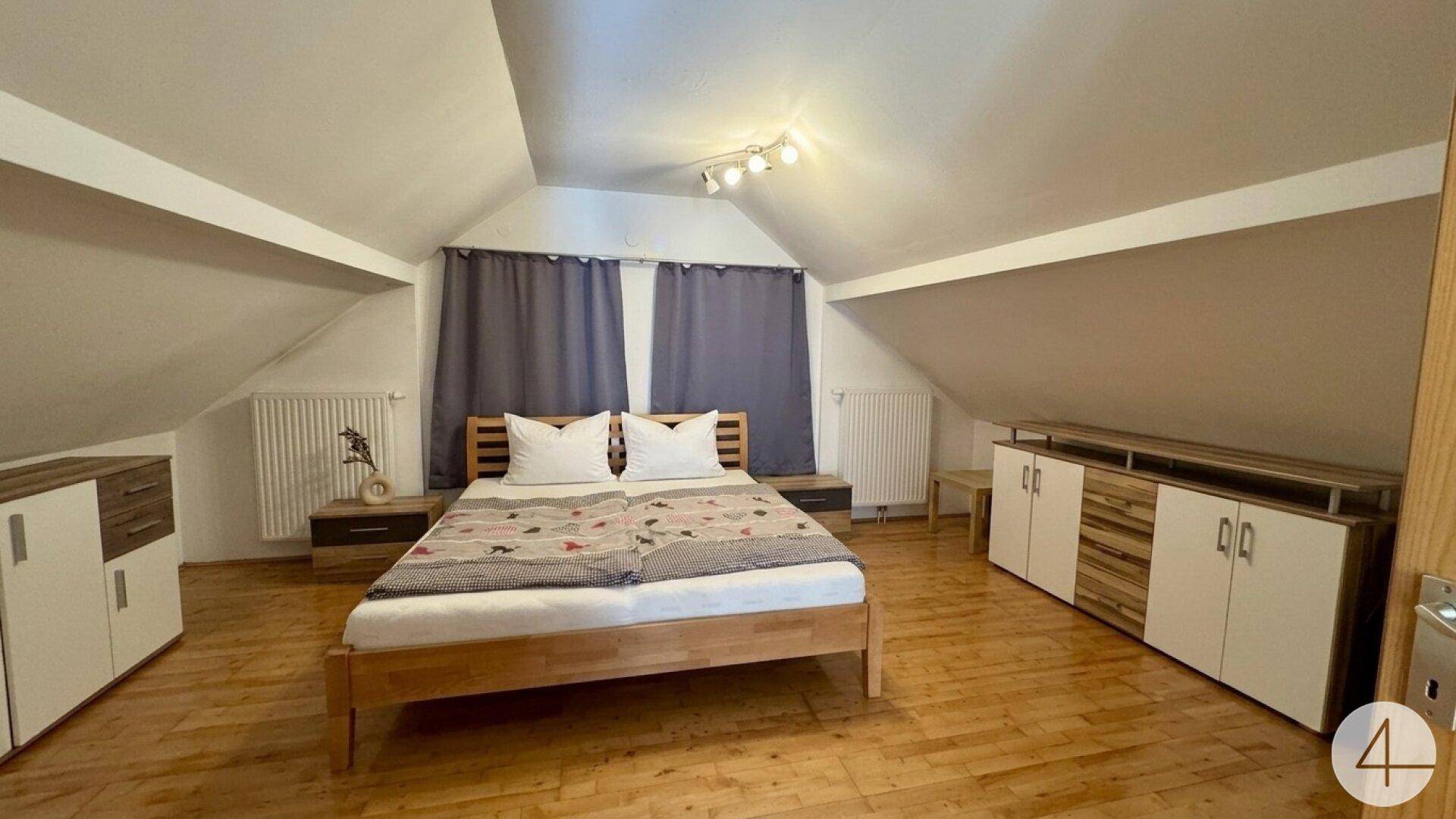 Schlafzimmer im Dachgeschoss mit Holzboden, Doppelbett und Dachschrägen.