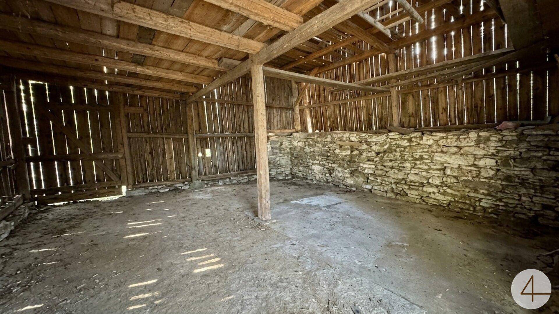 Rustikale Scheune mit Holzbalken, Steinmauern und Erdboden.