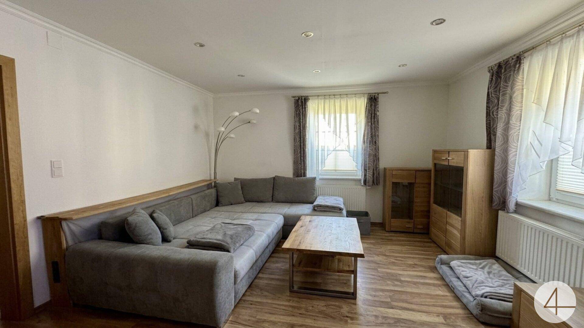 Helles Wohnzimmer mit großem Ecksofa, Holzboden und natürlichem Lichteinfall.