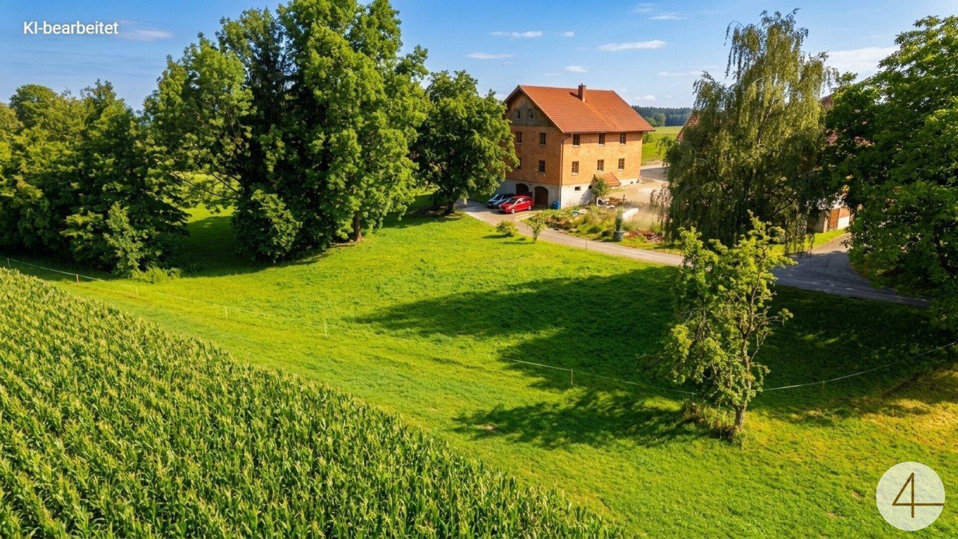 Haus in ländlicher Umgebung, umgeben von grünen Feldern und Bäumen unter blauem Himmel.