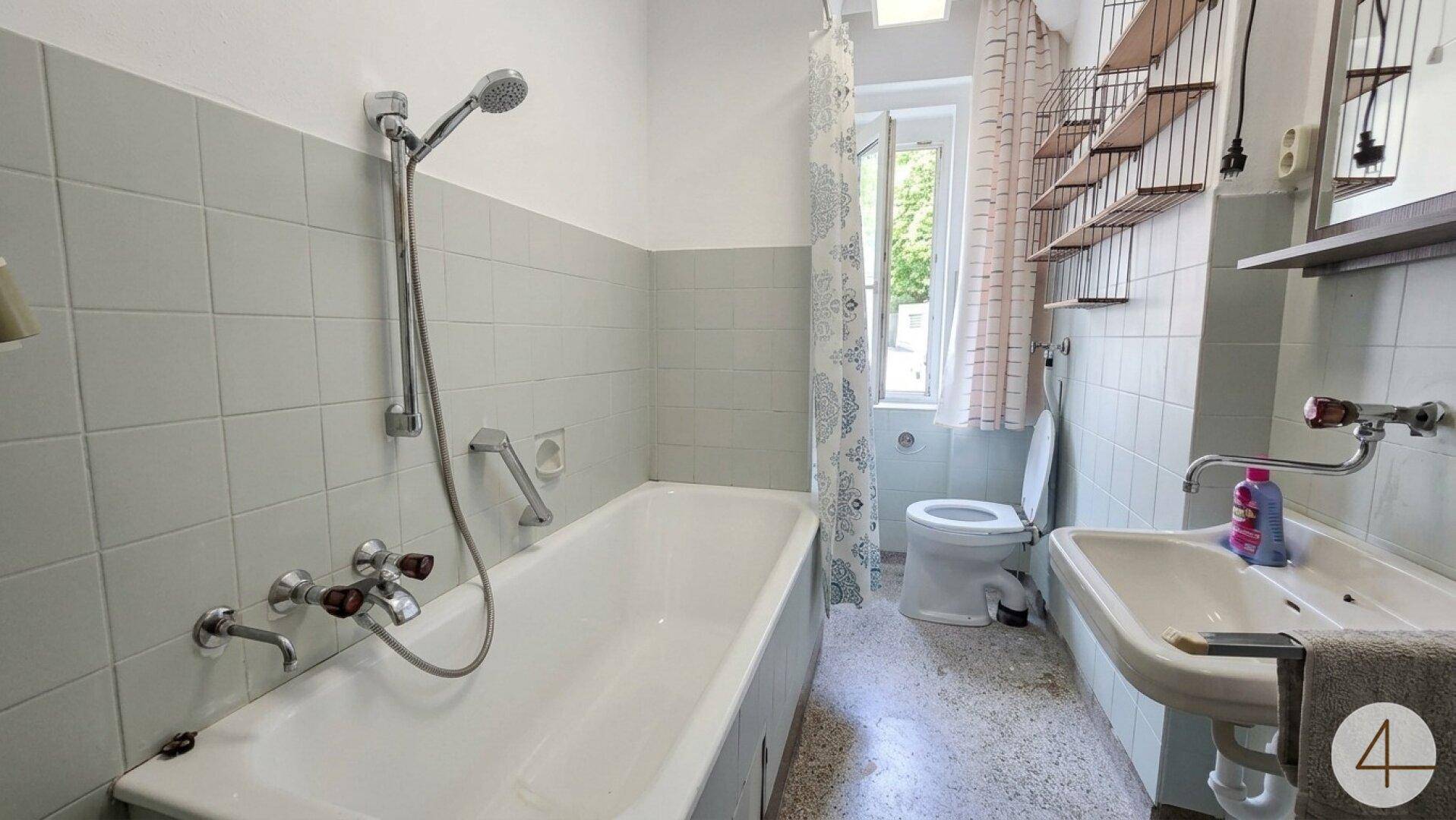 Badezimmer mit Badewanne, Waschbecken und WC, gefliest in hellem Grau.