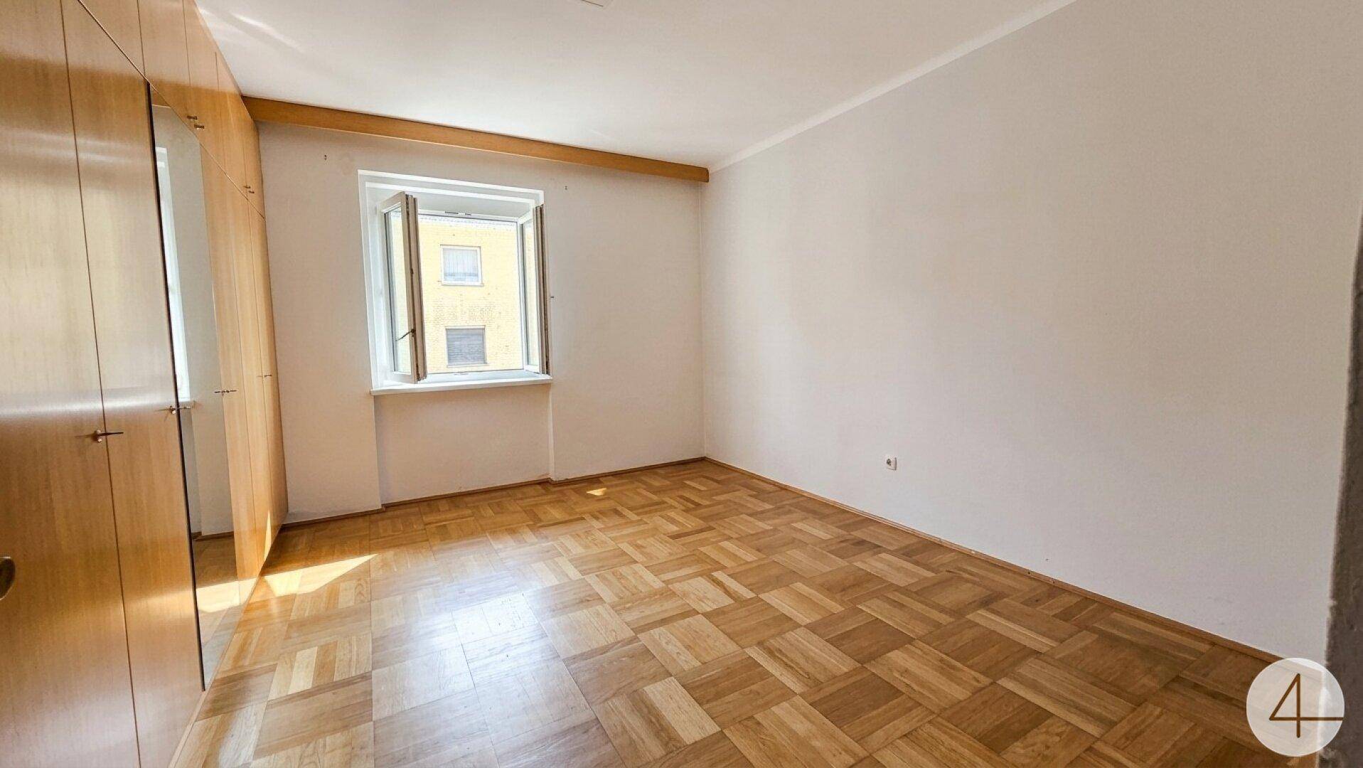 Helles Schlafzimmer mit Parkettboden, großem Kleiderschrank und Fenster.