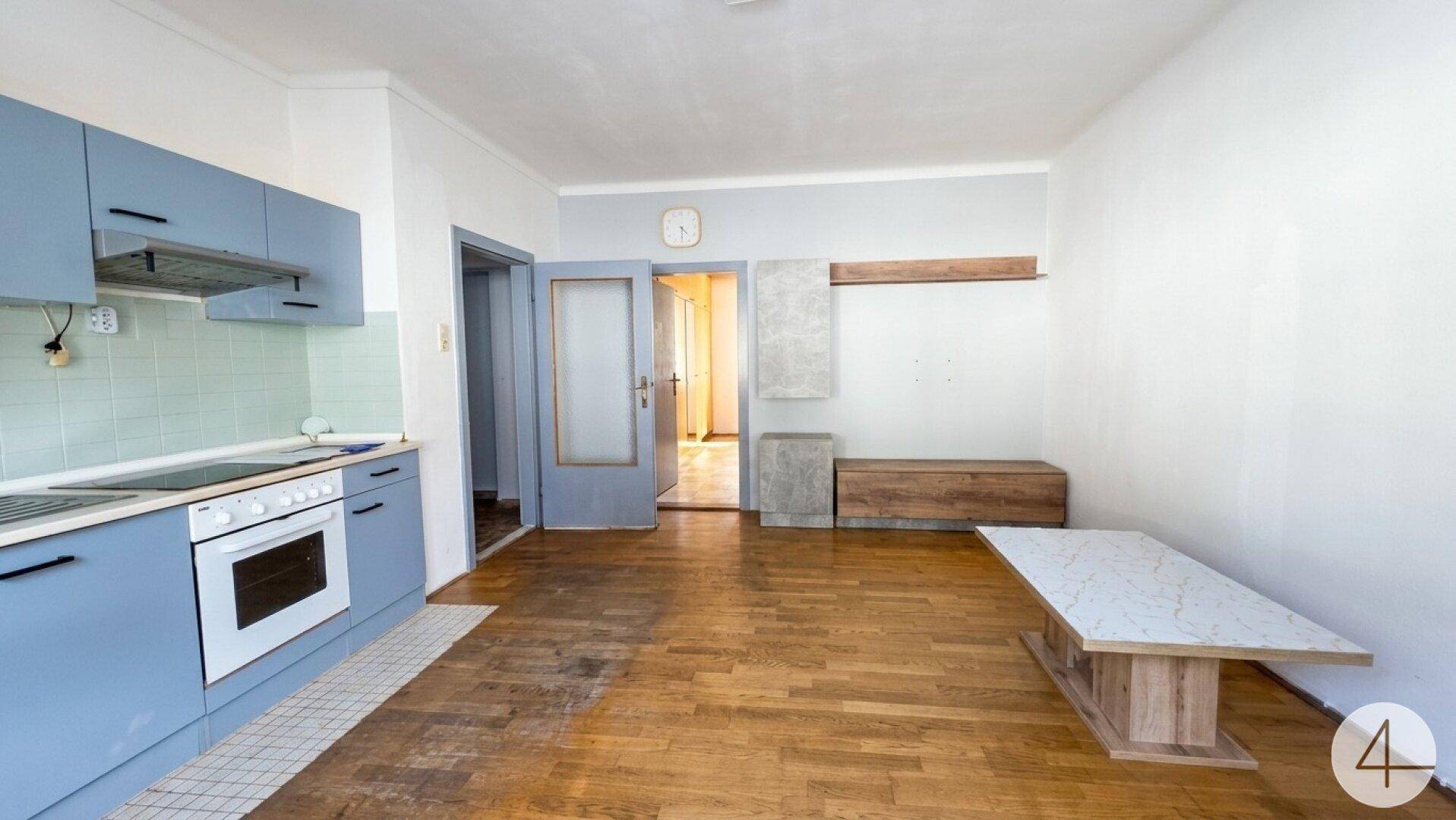 Blick vom Wohnbereich zur Küche und einem angrenzenden Flur mit Tür.