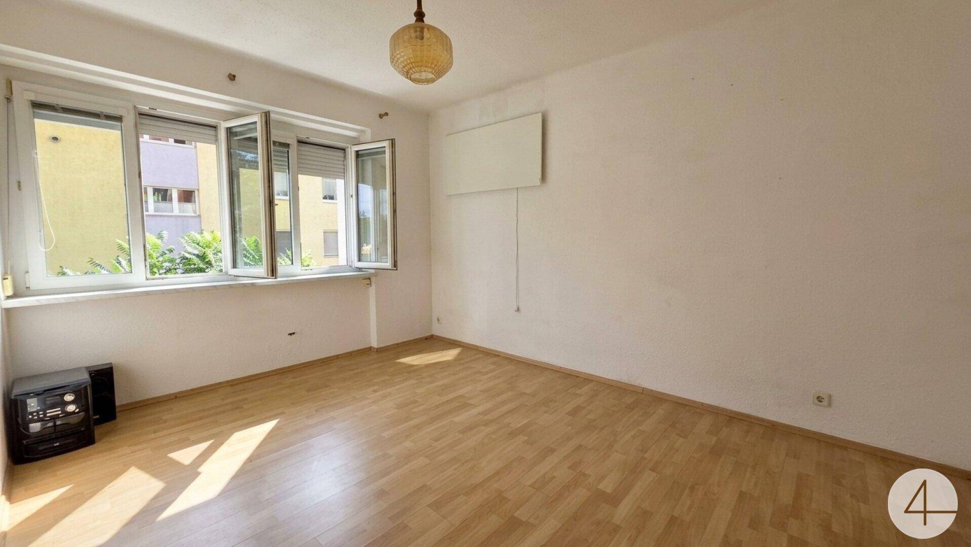 Leeres Zimmer mit Laminatboden, großen Fenstern und viel Tageslicht.