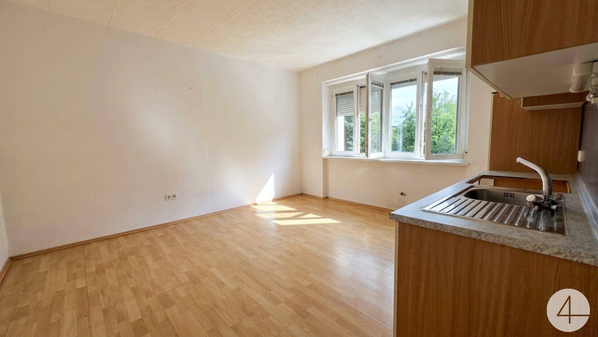 Heller Wohnbereich mit Laminatboden und einem Teil einer Küchenzeile.