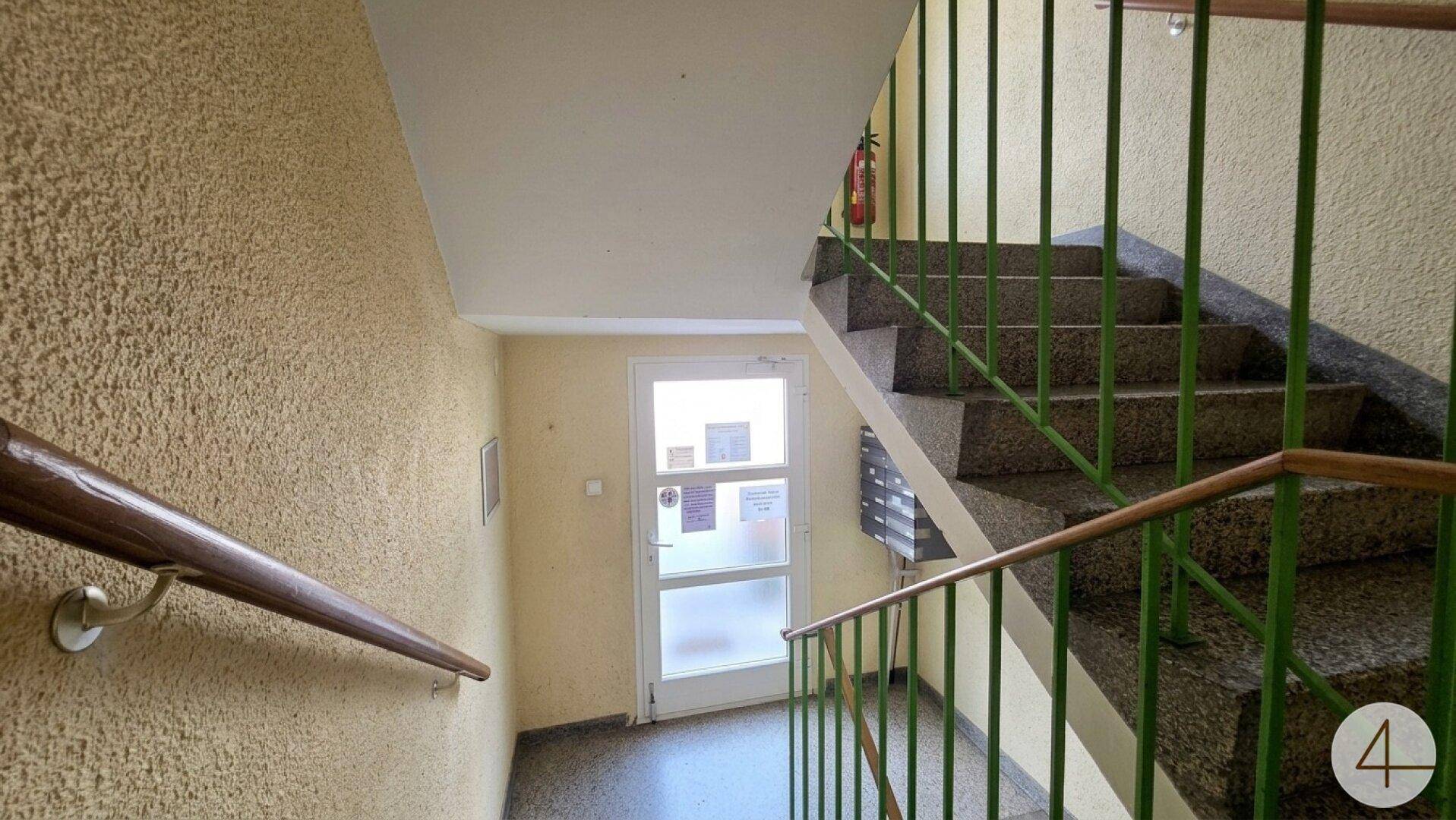 Treppenhaus mit Granitstufen und grünem Geländer in einem Mehrfamilienhaus.