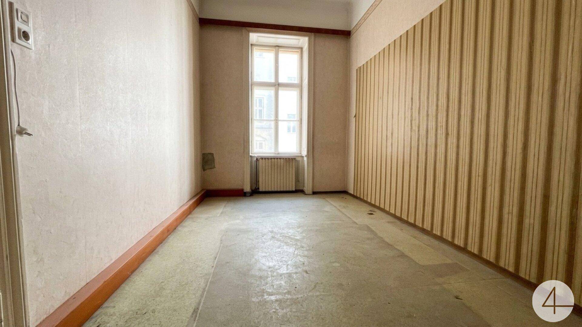 Heller, leerer Raum mit Fenster, alter Tapete und Heizkörper, bereit zur Renovierung.