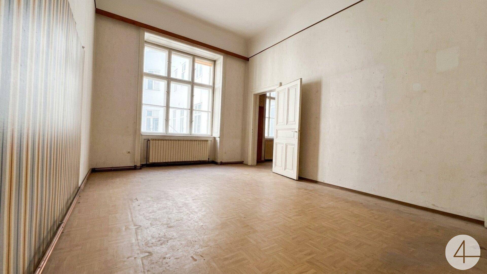 Geräumiger leerer Raum mit großem Fenster, altem Parkettboden und Heizkörper.