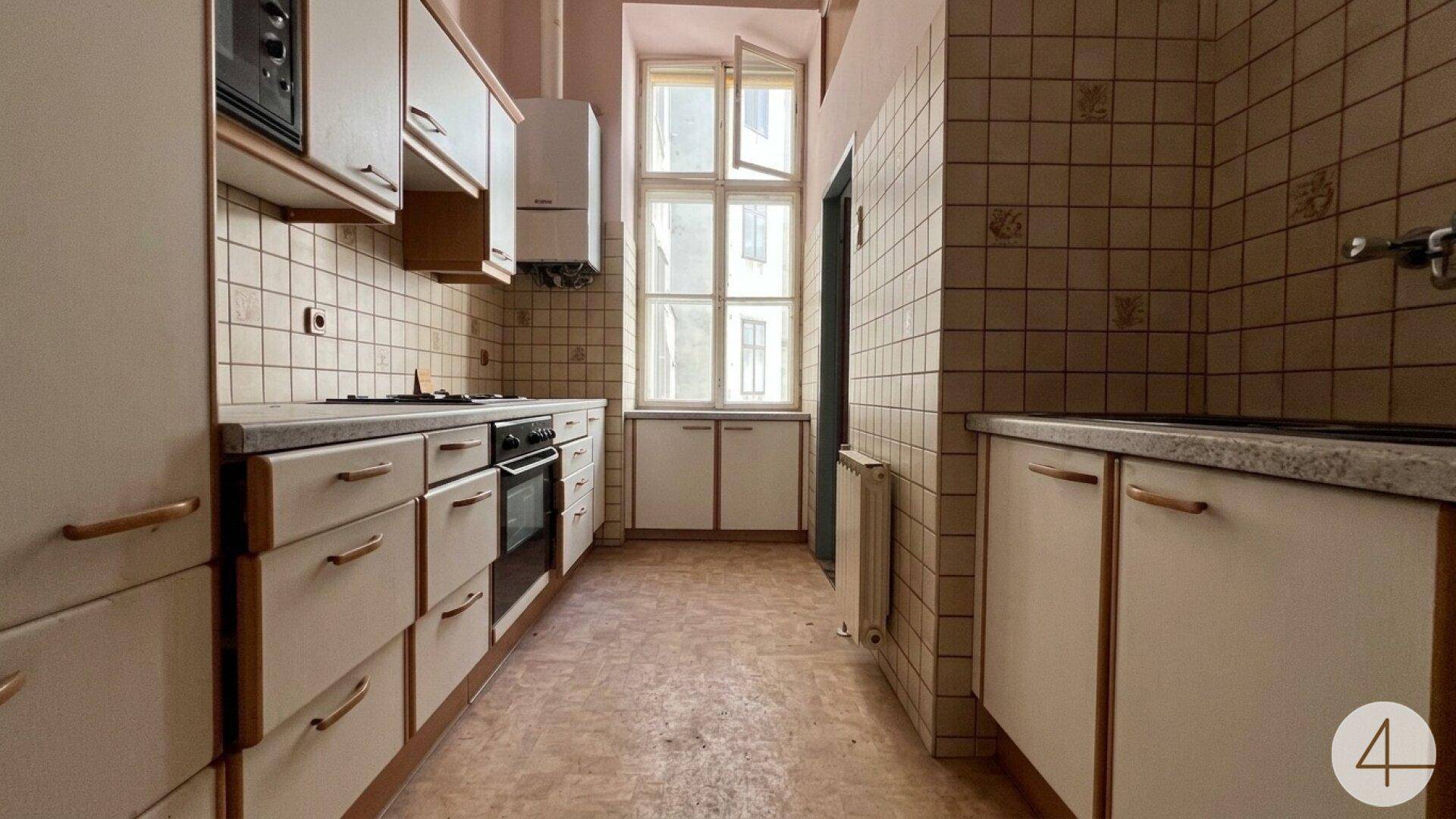 Funktionale Küche mit beigen Fliesen, weißen Schränken, Ofen und Mikrowelle, mit Fenster.