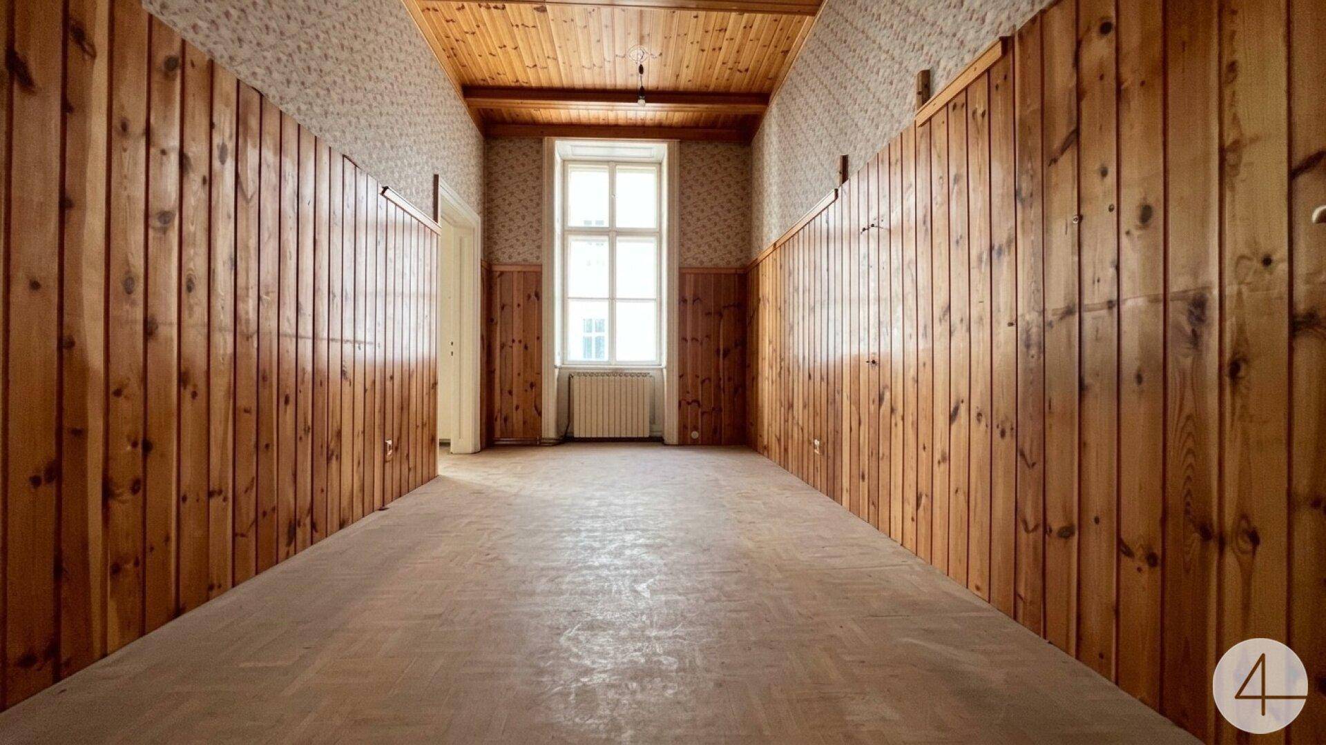 Langer Raum mit holzvertäfelten Wänden und Decke, einem Fenster am Ende und viel natürlichem Licht.