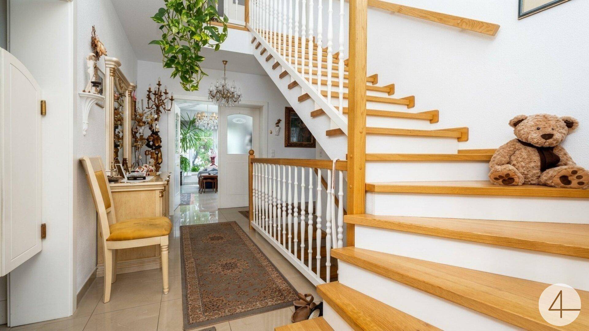 Heller Flur mit eleganter Holztreppe, gefliestem Boden und traditionellen Möbeln.
