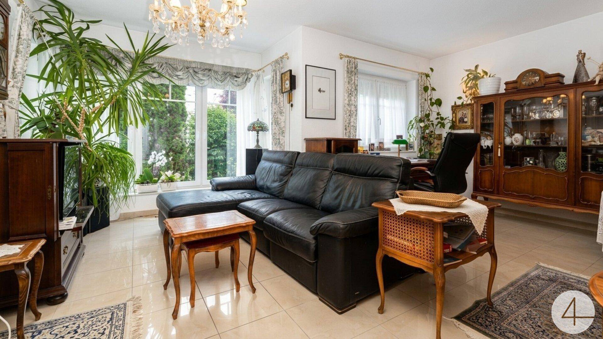 Gemütliches Wohnzimmer mit schwarzem Ledersofa, klassischen Holzmöbeln und gefliestem Boden.